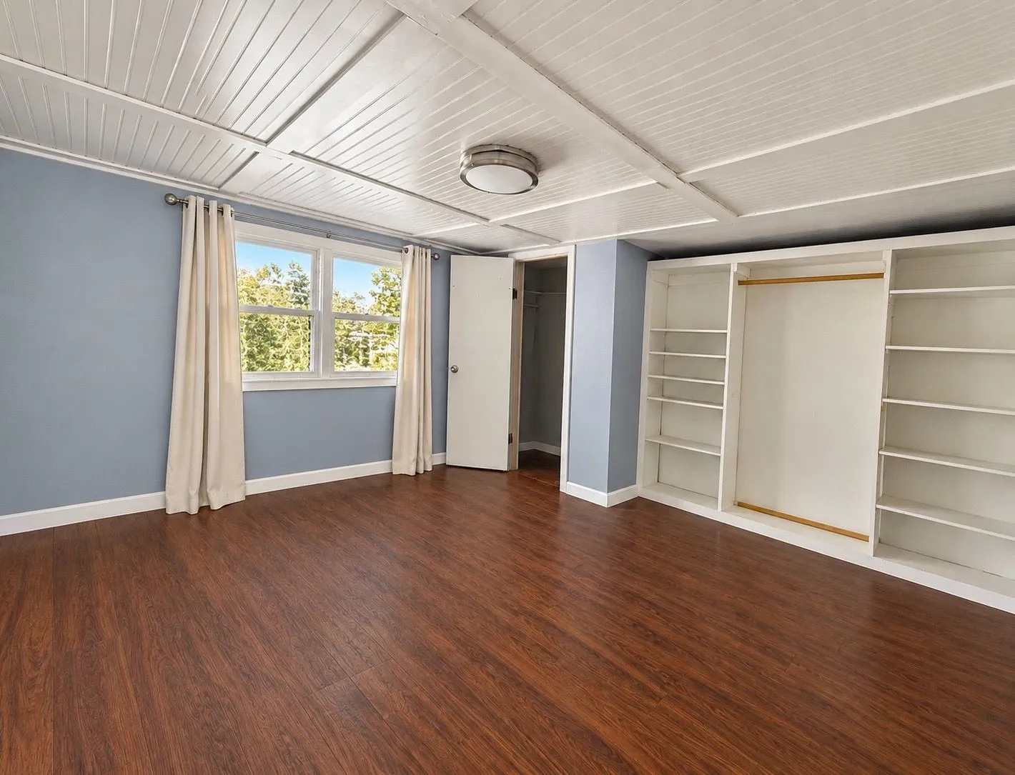 Wood-finish flooring, white beadboard ceiling, built-in shelving unit, and central flush-mount lighting fixture