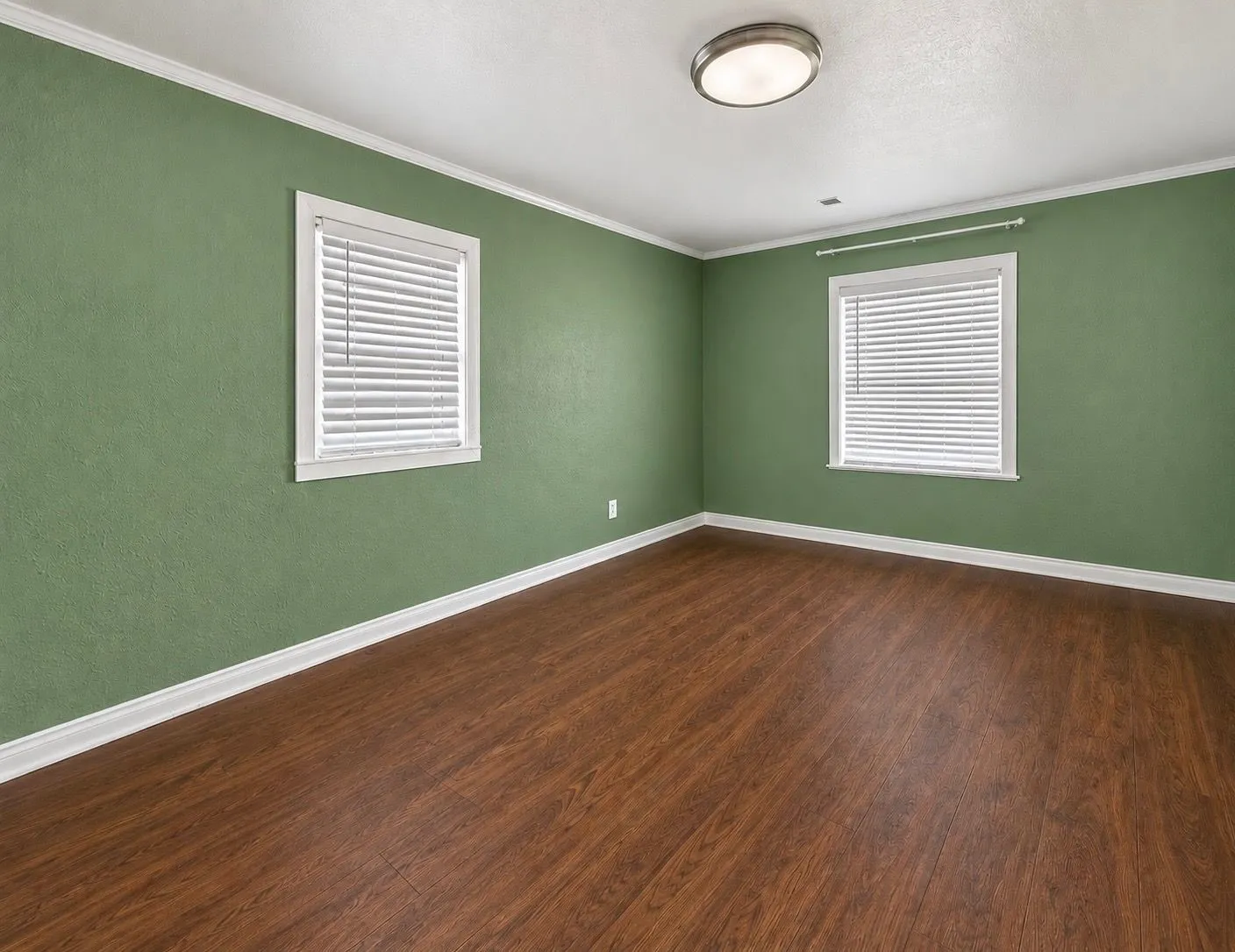 Room featuring wood-finish flooring, two windows with horizontal blinds, and a central flush-mount light fixture
