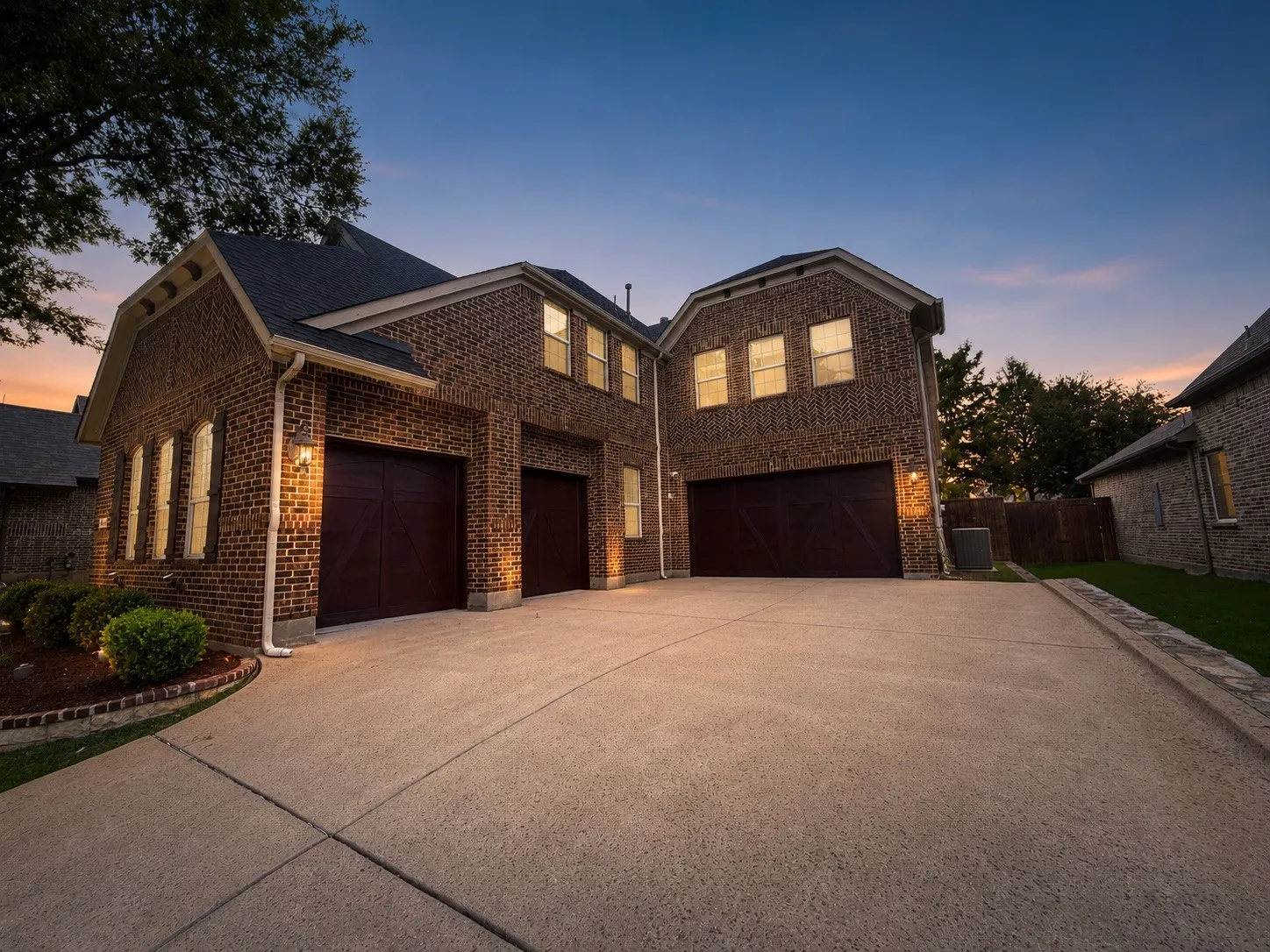 Brick exterior with multiple gabled rooflines, featuring dark wood garage doors and complementary exterior lighting