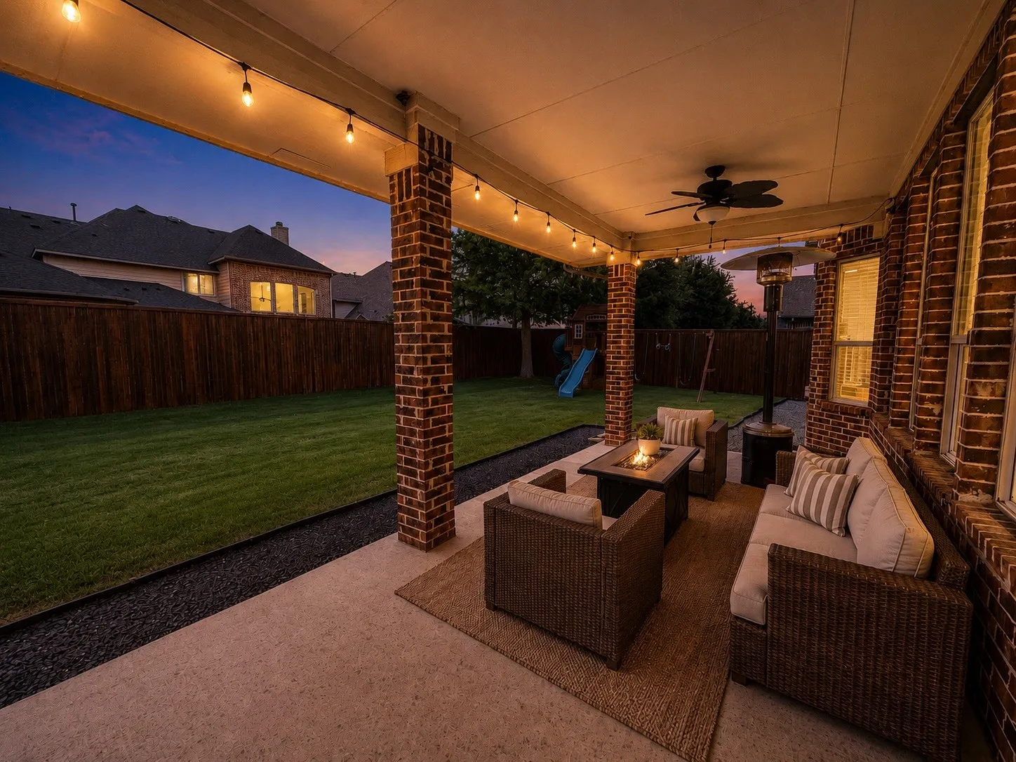 Covered patio featuring brick pillars, string lighting, and a ceiling fan