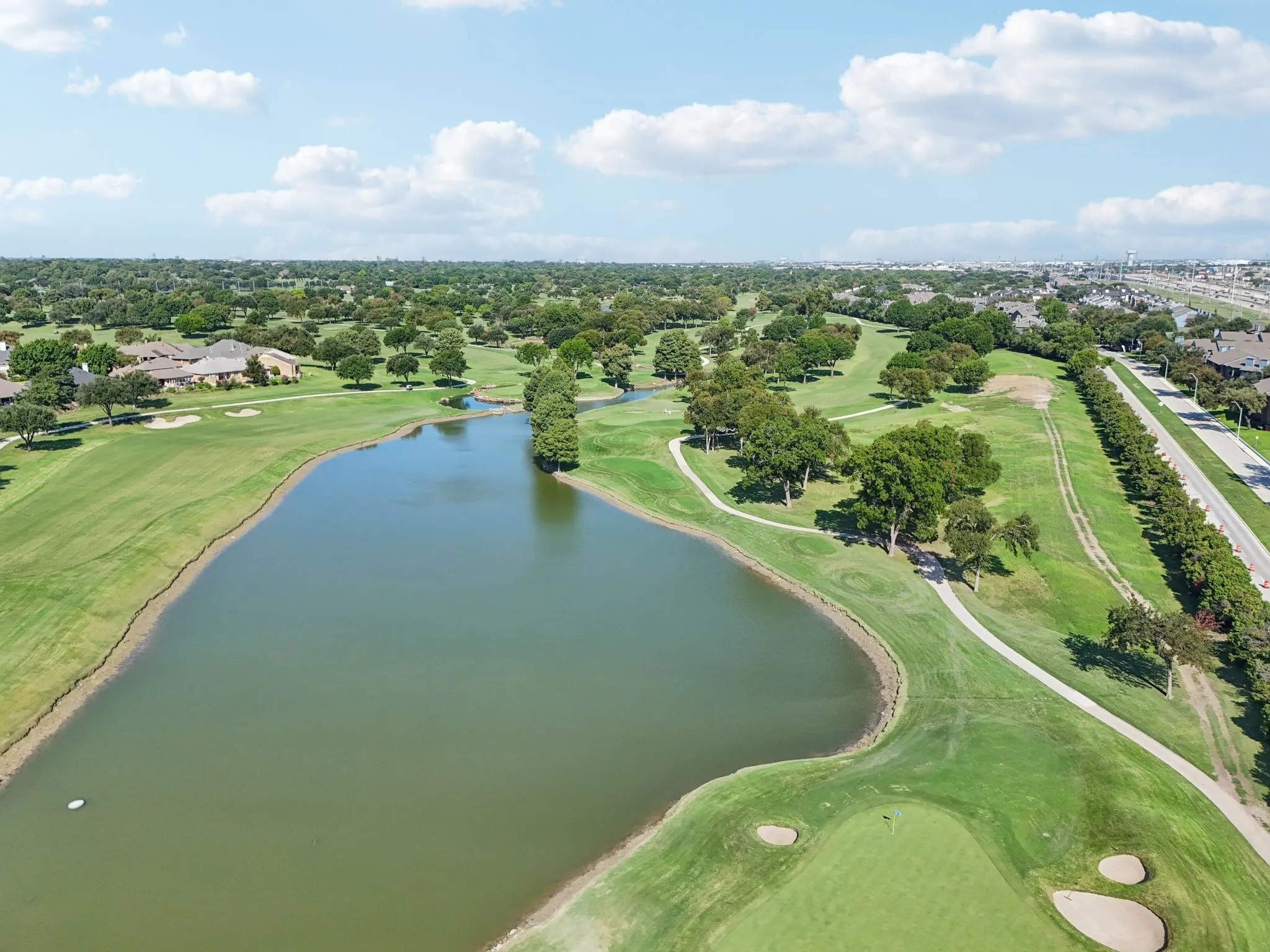Expansive golf course setting featuring a sizable pond, manicured greens, sand traps, and mature trees