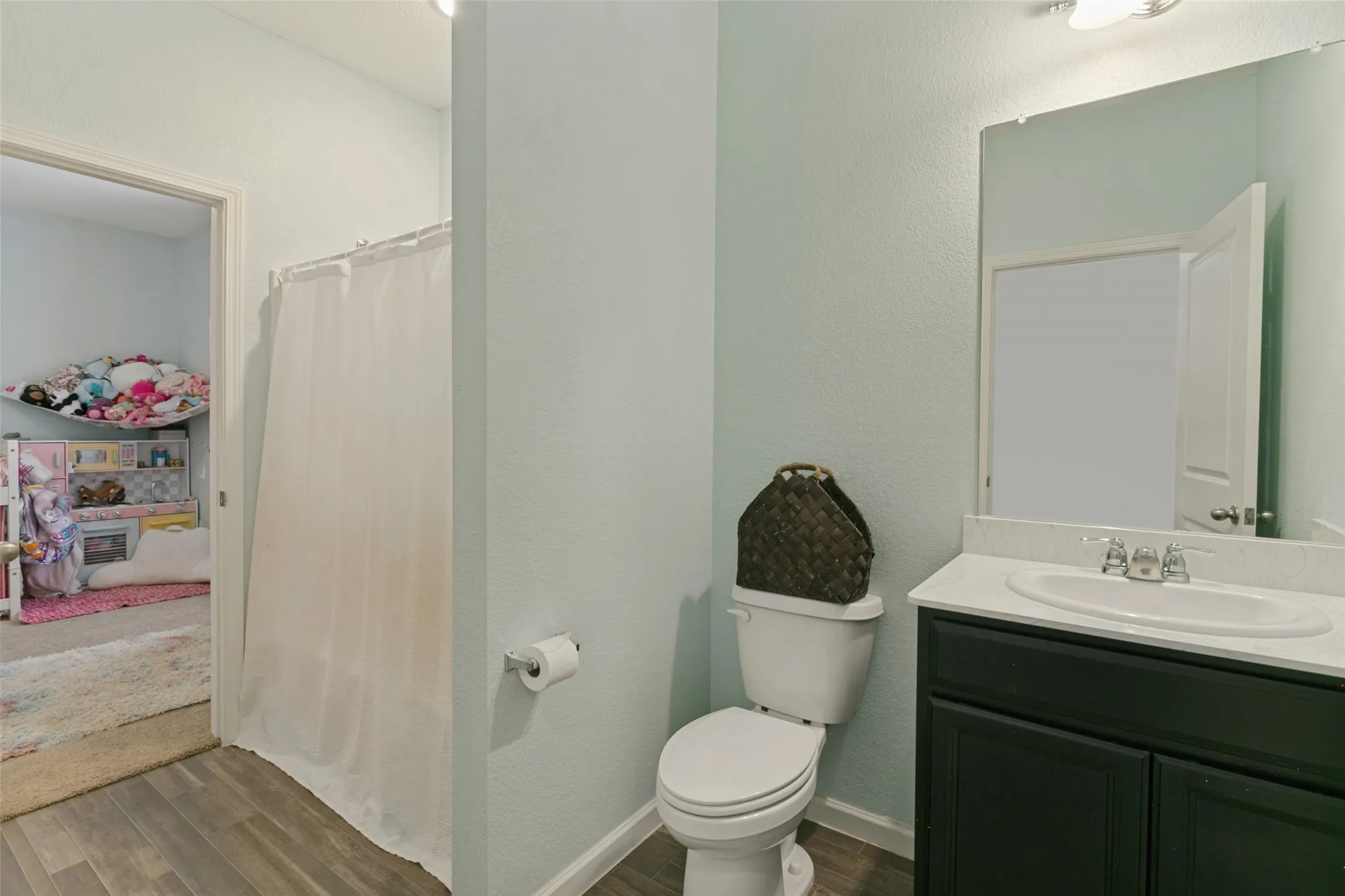 Bathroom featuring a vanity with a white countertop and oval sink, a wall-mounted mirror, and wood-finish flooring