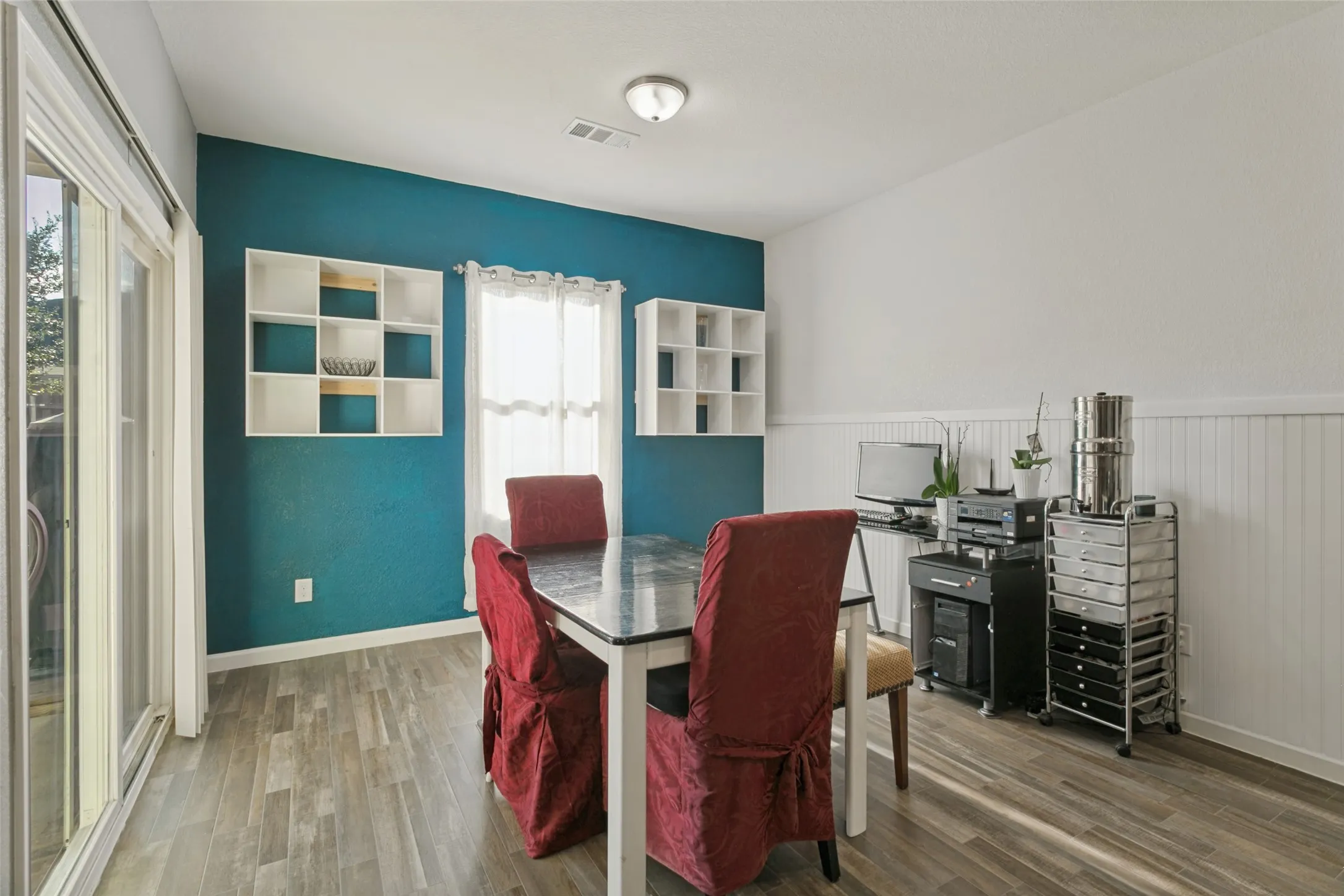 Wood-finish flooring, dual built-in wall shelving units, sliding glass door, and white wainscoting