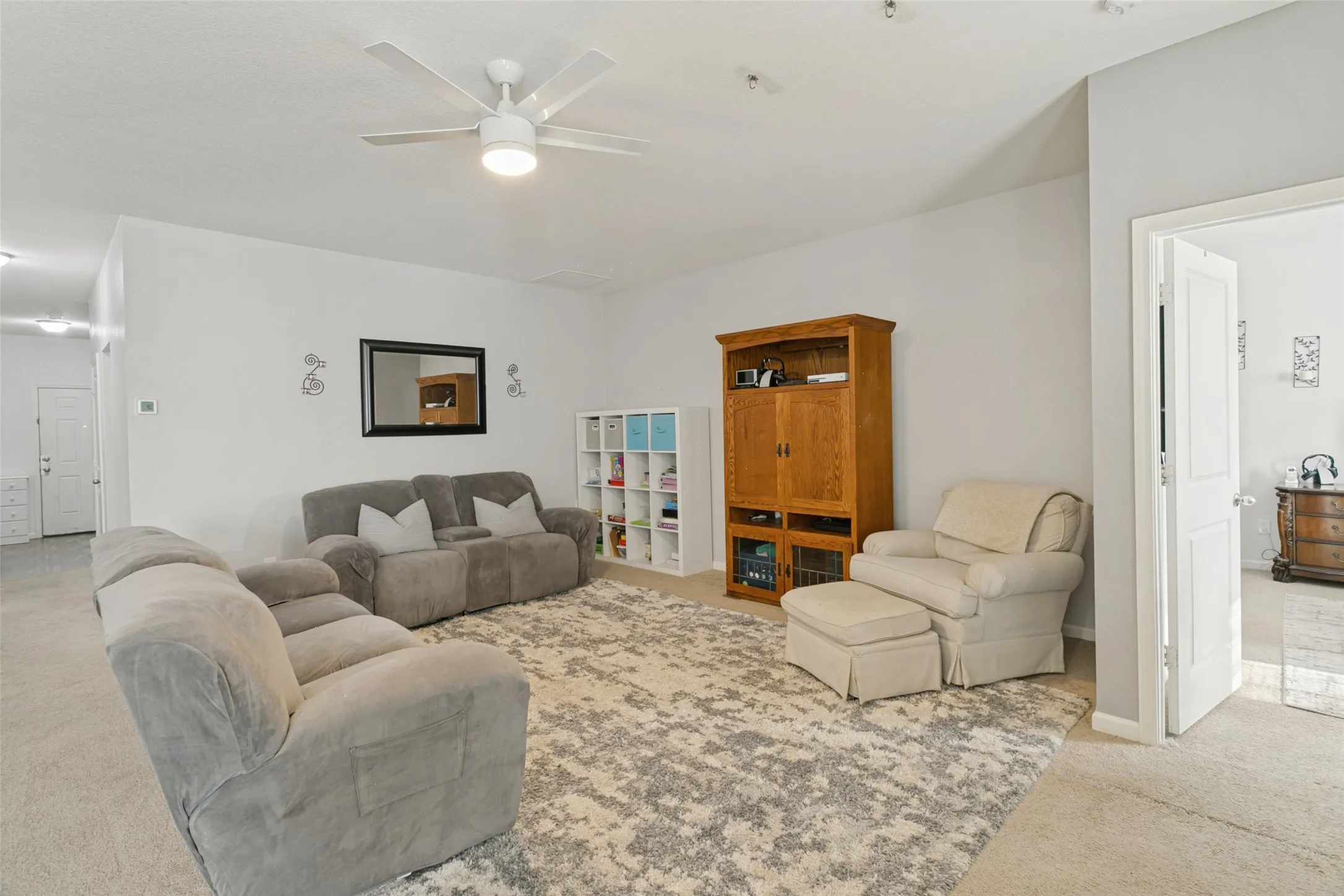 Living area featuring neutral wall paint, carpeting, and a white ceiling fan with integrated lighting