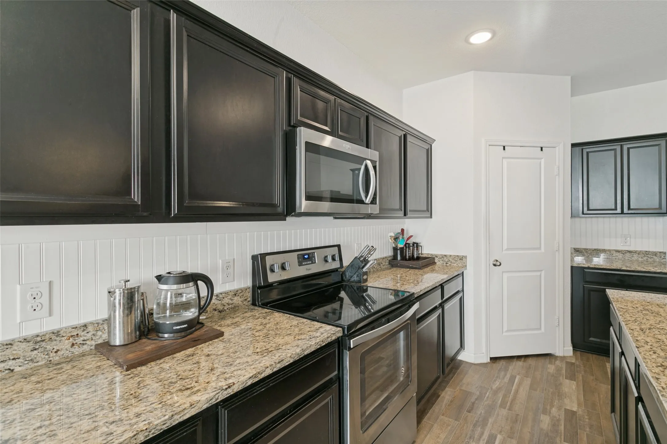 Kitchen featuring black cabinetry, stone-finish countertops, beadboard backsplash, stainless steel appliances, and wood-finish flooring