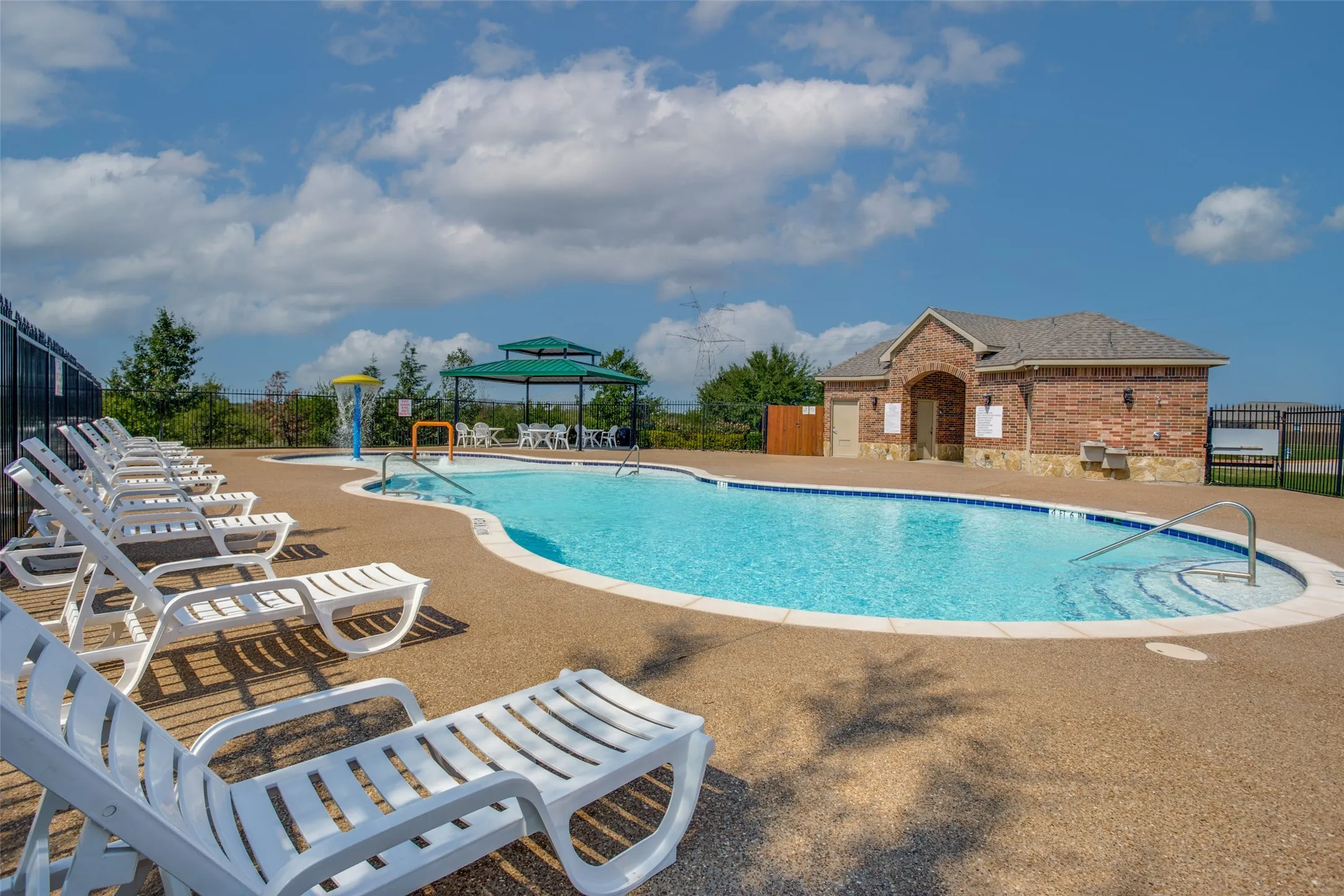 Swimming pool with an integrated water feature, sprawling concrete deck, covered gazebo, and a brick clubhouse