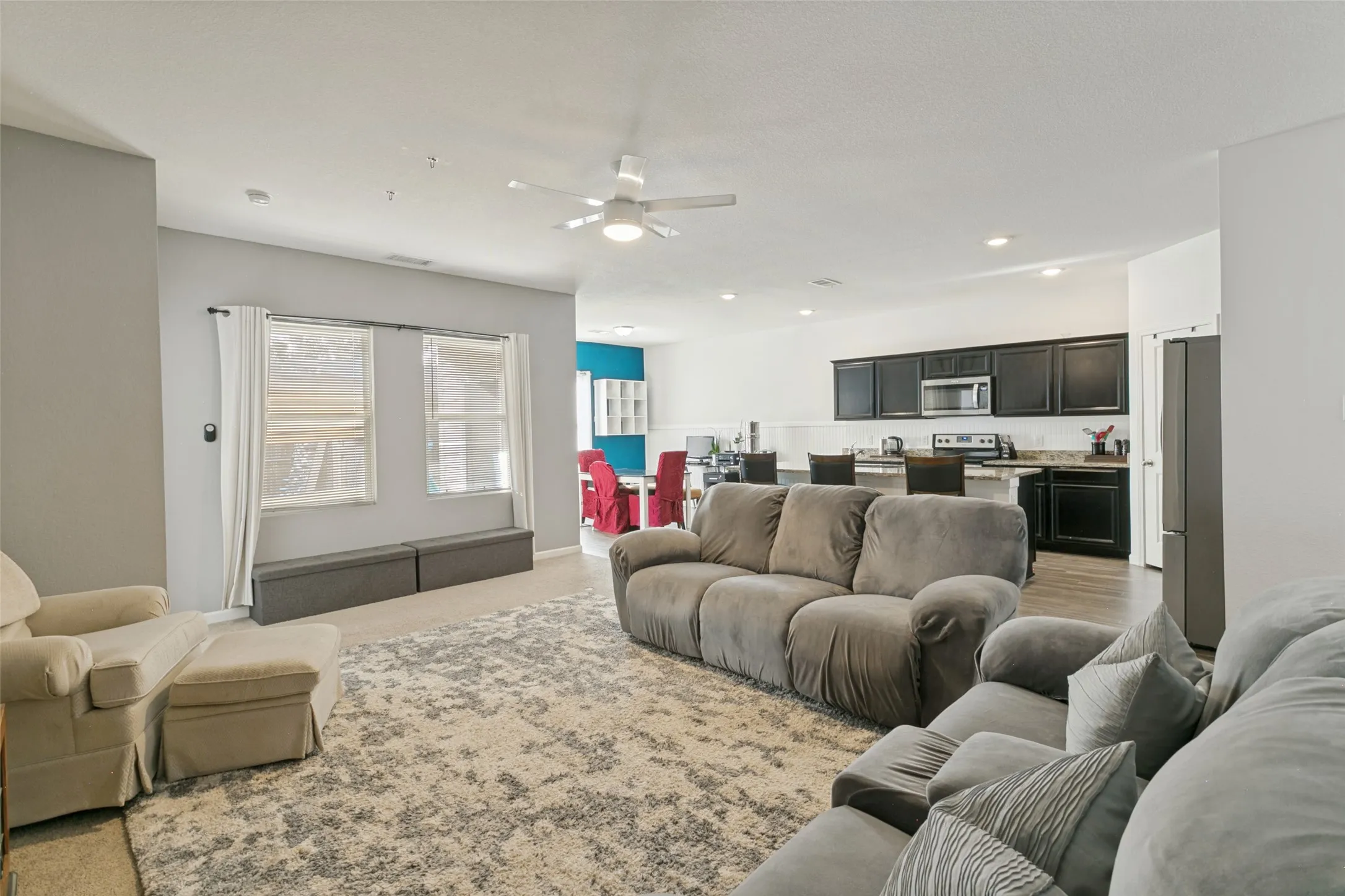 Open-concept floor plan featuring recessed lighting, a ceiling fan, and a kitchen equipped with dark cabinetry, a breakfast bar, and stainless steel appliances