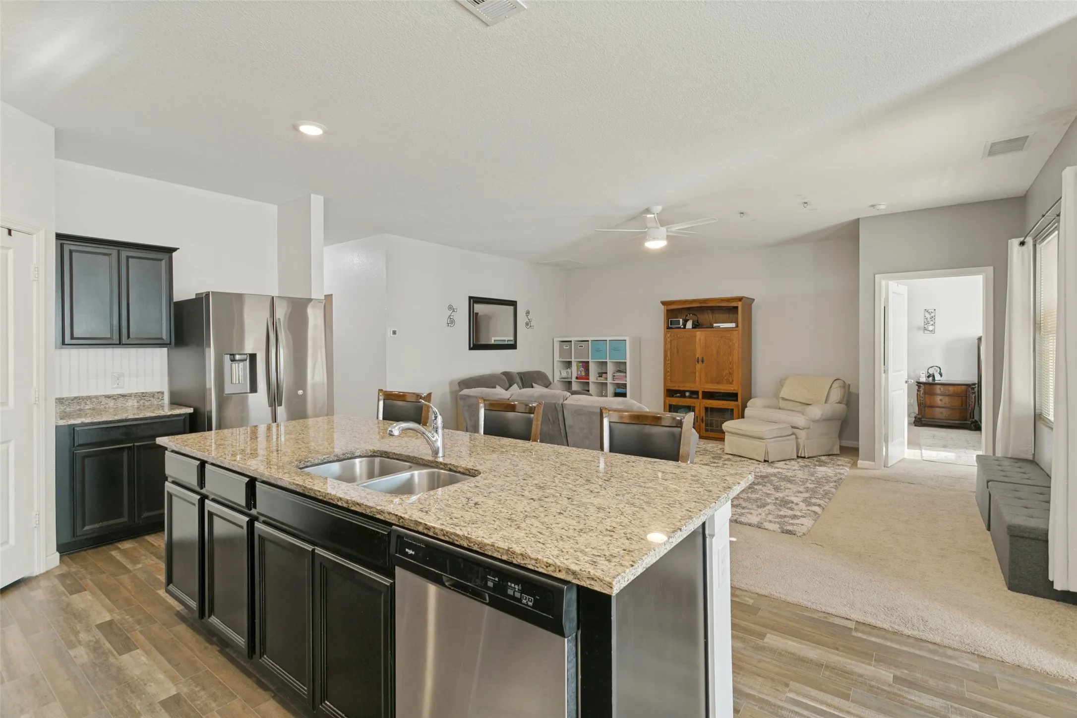 Kitchen featuring a center island with a dual-basin stainless steel sink, granite countertops, dark-finish cabinetry, stainless steel appliances, and wood-finish flooring