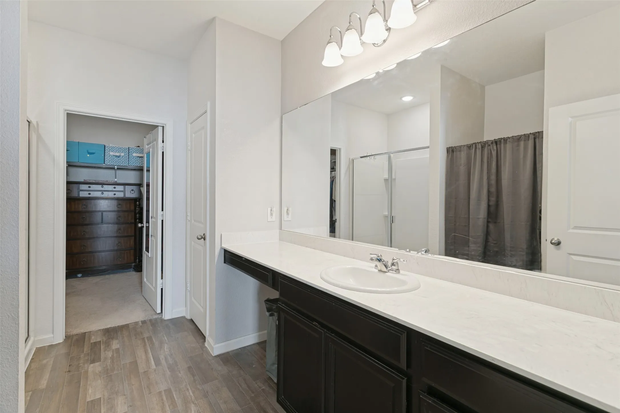 Bathroom vanity featuring dark-toned cabinetry, a light-colored countertop, an oval undermount sink, a full-width mirror, and multi-bulb wall lighting