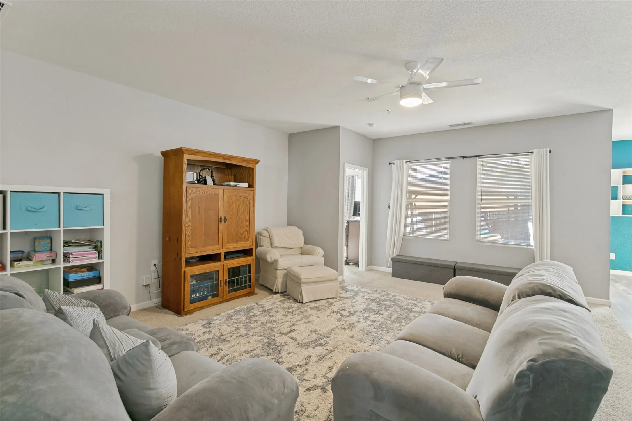 Living area featuring neutral wall paint, carpeting, dual windows, and a ceiling fan with integrated lighting