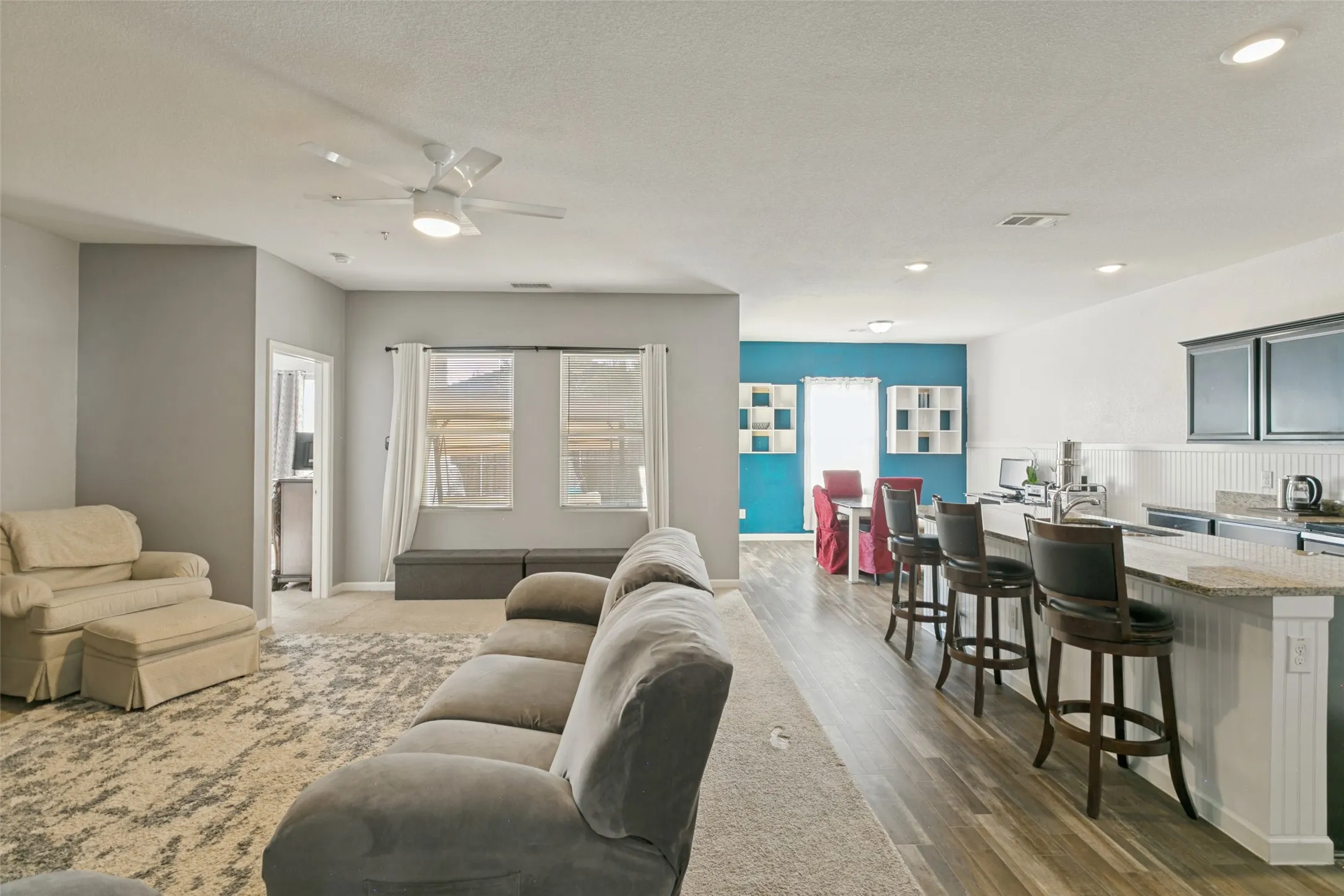 Open-concept living space featuring wood-finish flooring, a kitchen peninsula with stone-finish countertops, recessed lighting, and a ceiling fan