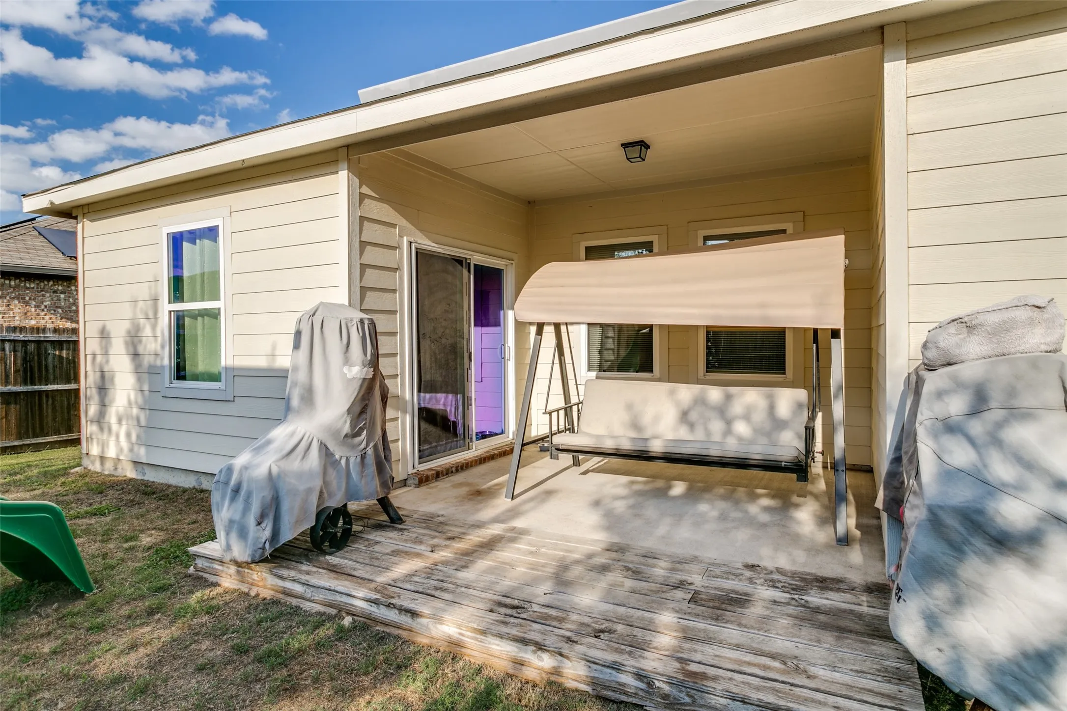 Covered concrete patio with horizontal siding, sliding glass door access, and exterior wall-mounted lighting
