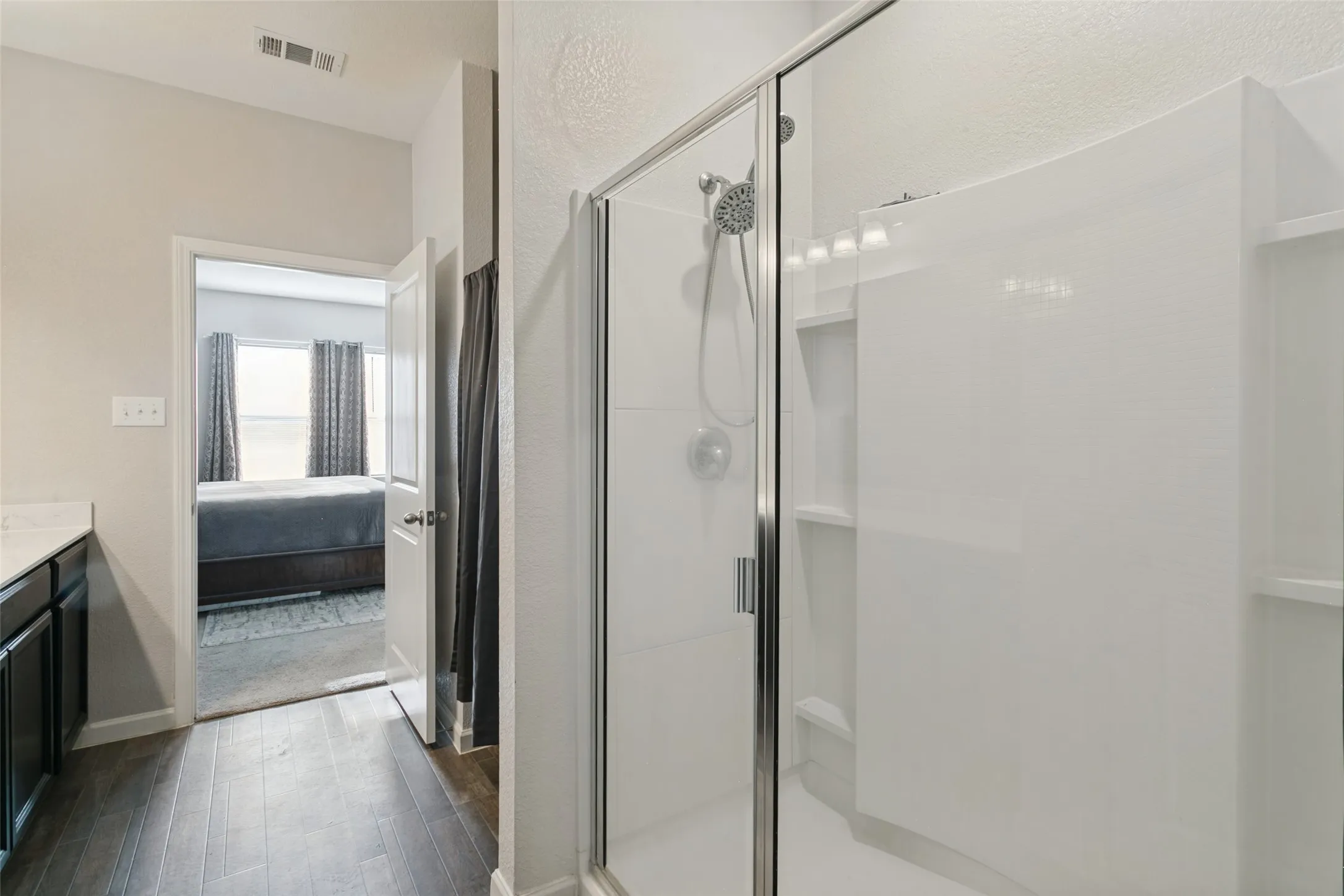 Walk-in shower with white surround, glass enclosure, and multi-setting shower head, paired with dark wood-finish cabinetry and a light-toned countertop