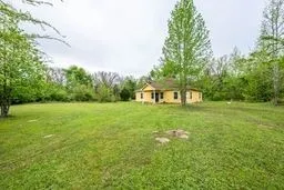 Single-story exterior with a covered entryway, sprawling acreage, and mature trees