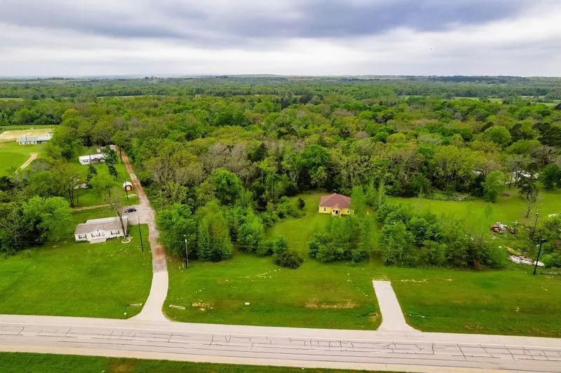 Aerial perspective of expansive acreage featuring a detached residential structure, mature timber, open grass expanses, and private paved driveway access