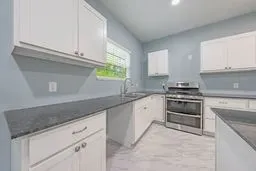 Kitchen featuring white cabinetry, dark stone countertops, stainless steel dual-oven range, and light-toned patterned flooring