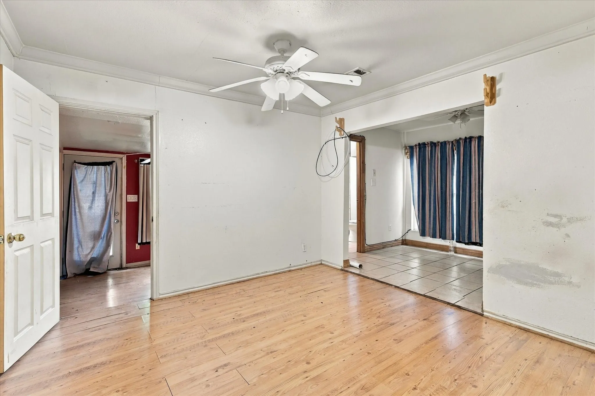 Interior space featuring wood-finish flooring, a ceiling fan with integrated light fixture, crown molding, and tiled flooring in the secondary area