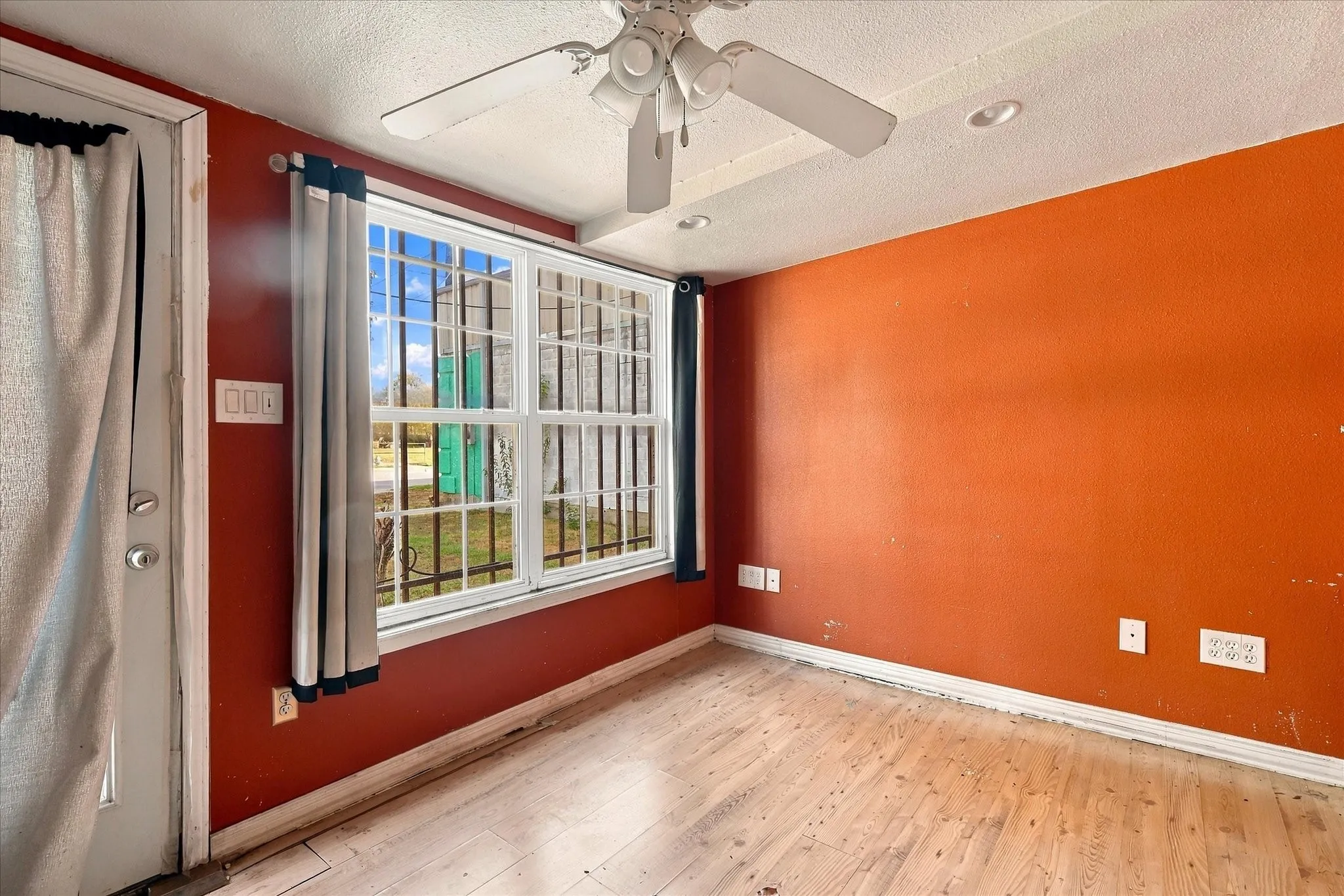 Room featuring wood-finish flooring, a multi-pane window with exterior security bars, a ceiling-mounted fan with integrated lighting, and recessed ceiling lights