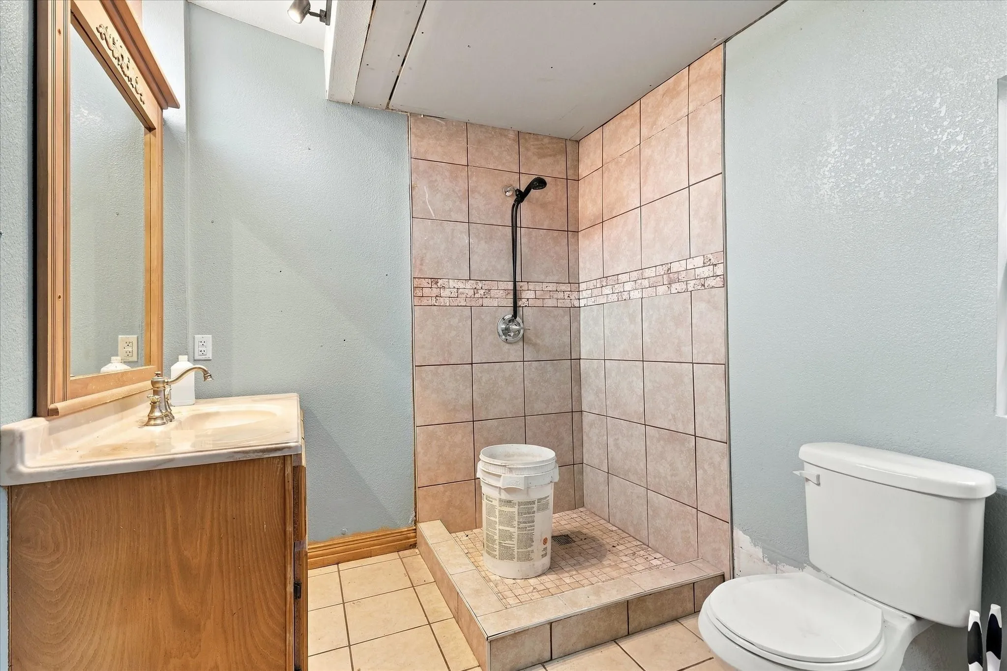 Bathroom featuring a wooden vanity, integrated basin, wall-mounted mirror, walk-in shower with tile surround and decorative accent inlay, and a standard toilet