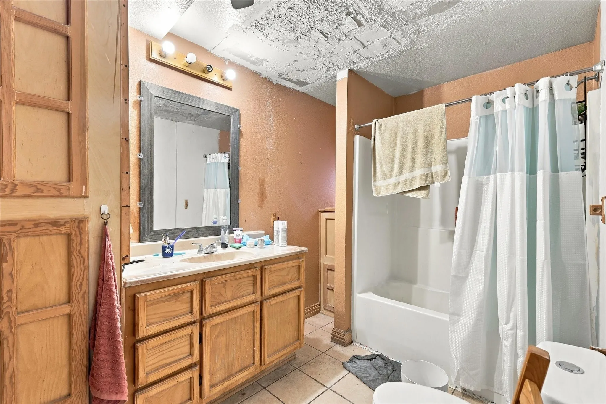 Bathroom featuring a natural wood-finish vanity, stone-pattern countertop, framed wall mirror, and a white tub-shower combination with tile flooring