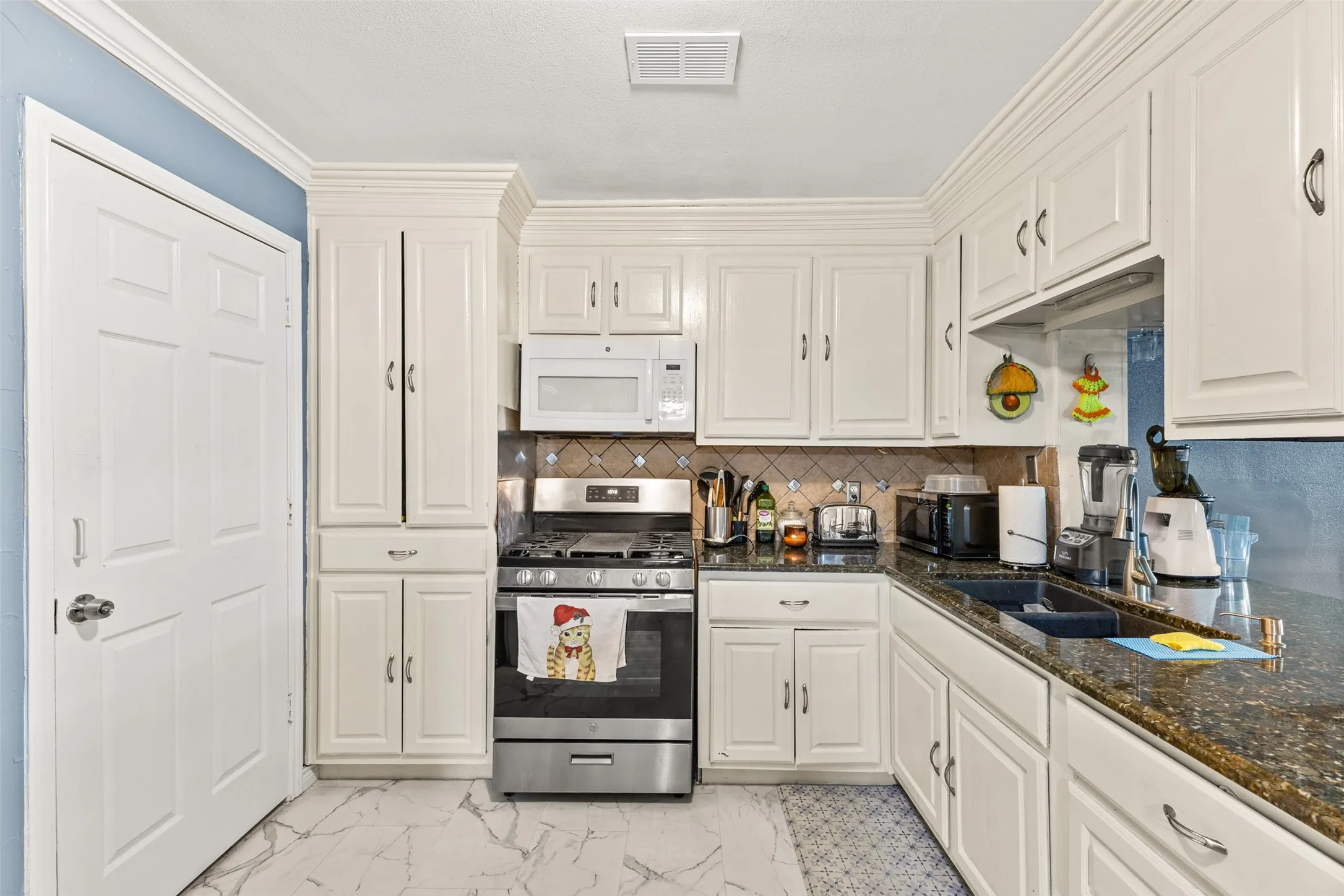 Kitchen featuring white cabinetry, stone-finish countertops, stainless steel gas range, built-in microwave, and tile backsplash