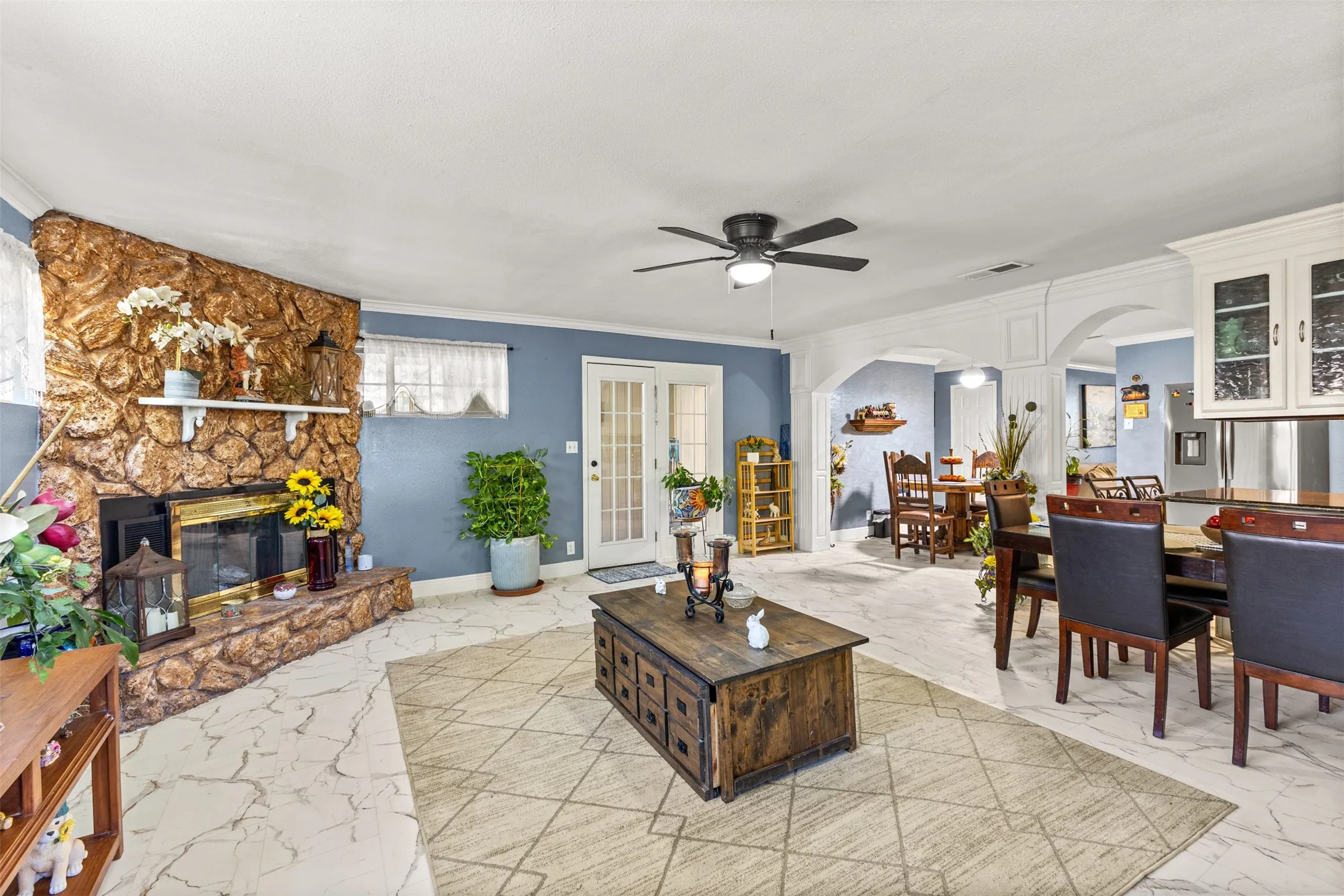 Stone fireplace with an integrated mantel, arched architectural detailing, tile flooring, glass-paneled exterior door, and built-in upper cabinetry