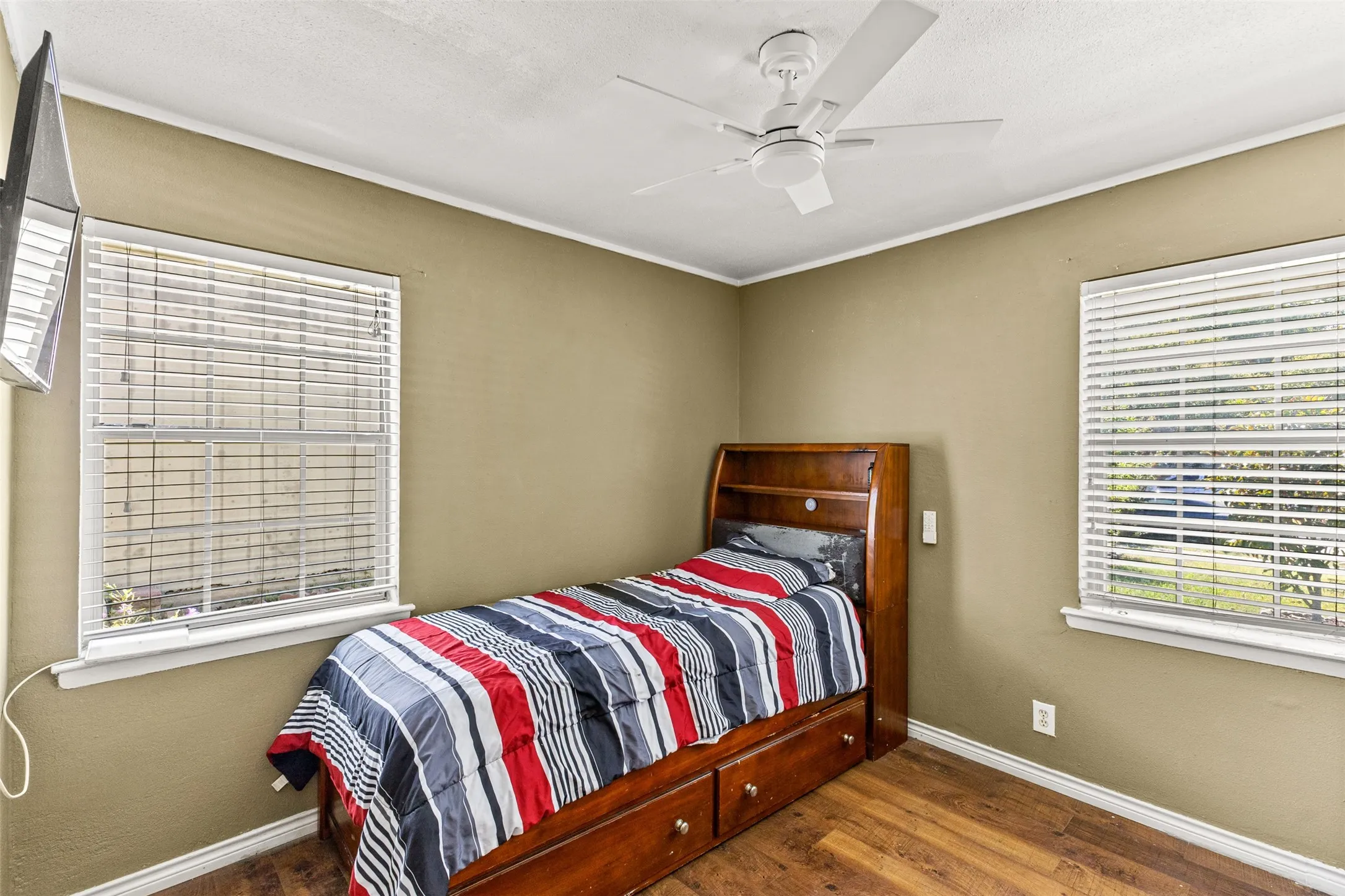 Interior room featuring wood-finish flooring, two dual-pane windows with horizontal blinds, and a white ceiling fan with integrated lighting