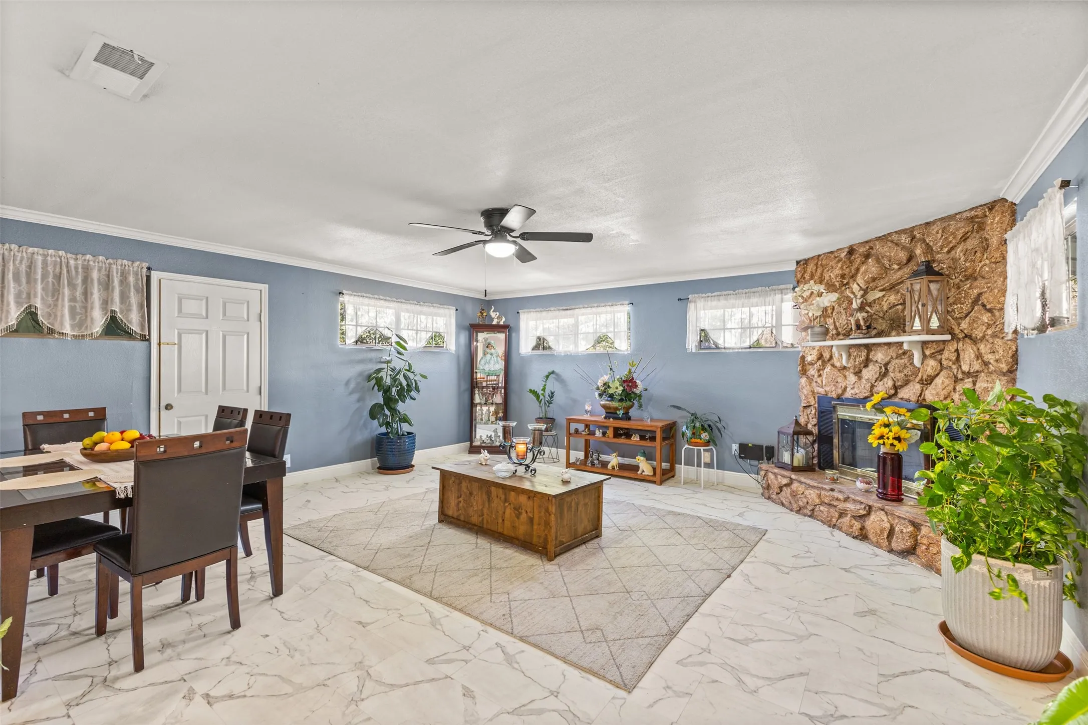 Living area featuring large-format tile flooring, a floor-to-ceiling fieldstone fireplace with a mantel, crown molding, and a ceiling fan