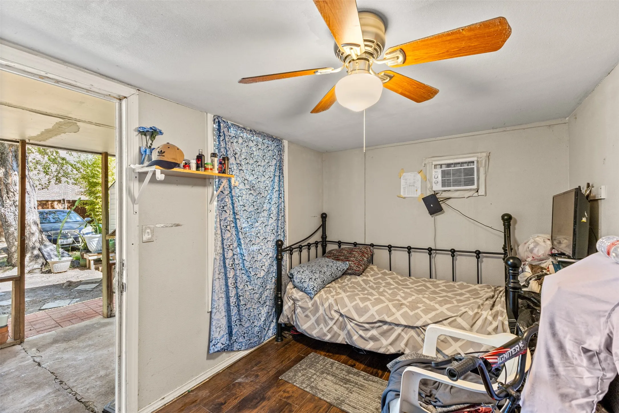 Room featuring wood-finish flooring, a wall-mounted cooling unit, a ceiling fan with integrated lighting, and an installed wall-mounted shelf