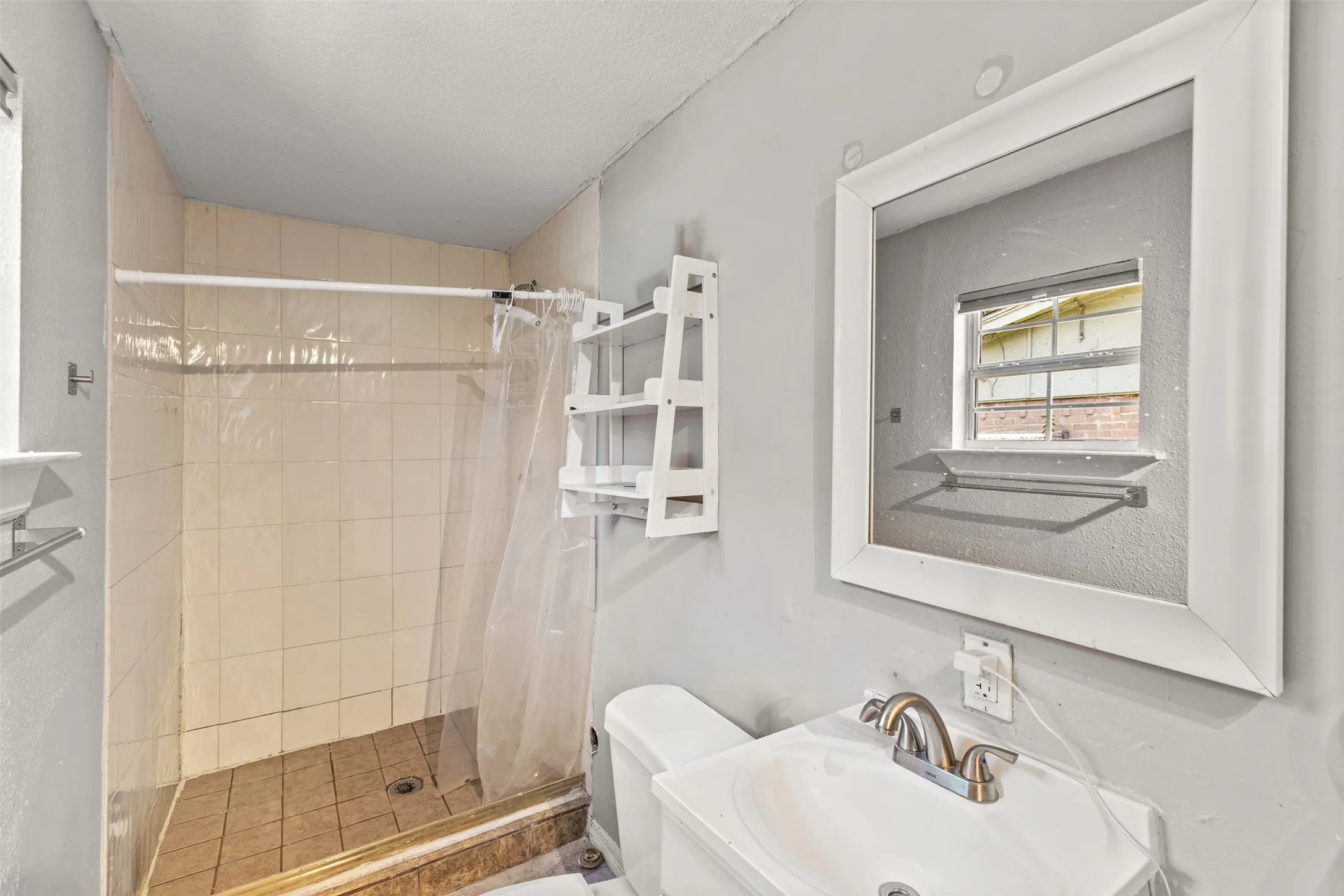 Bathroom featuring a pedestal sink, metallic dual-handle faucet, tiled shower surround, square wall mirror, and built-in shelving