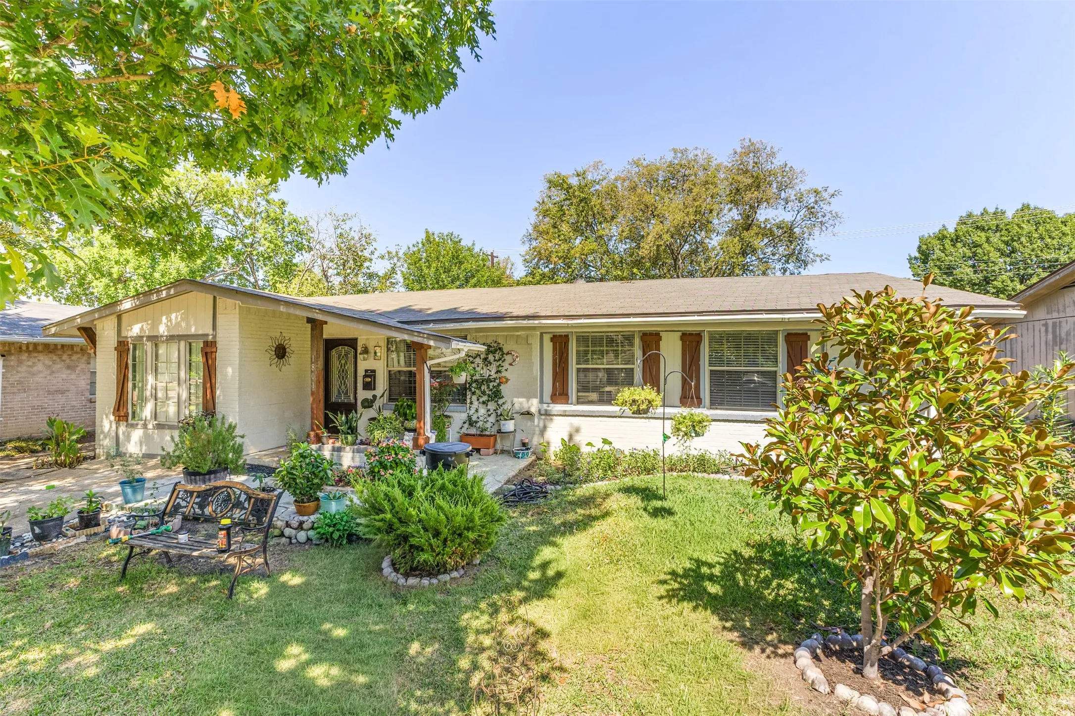Single-story residence featuring a painted masonry exterior, horizontal window shutters, covered front porch, and expansive front yard with mature landscaping