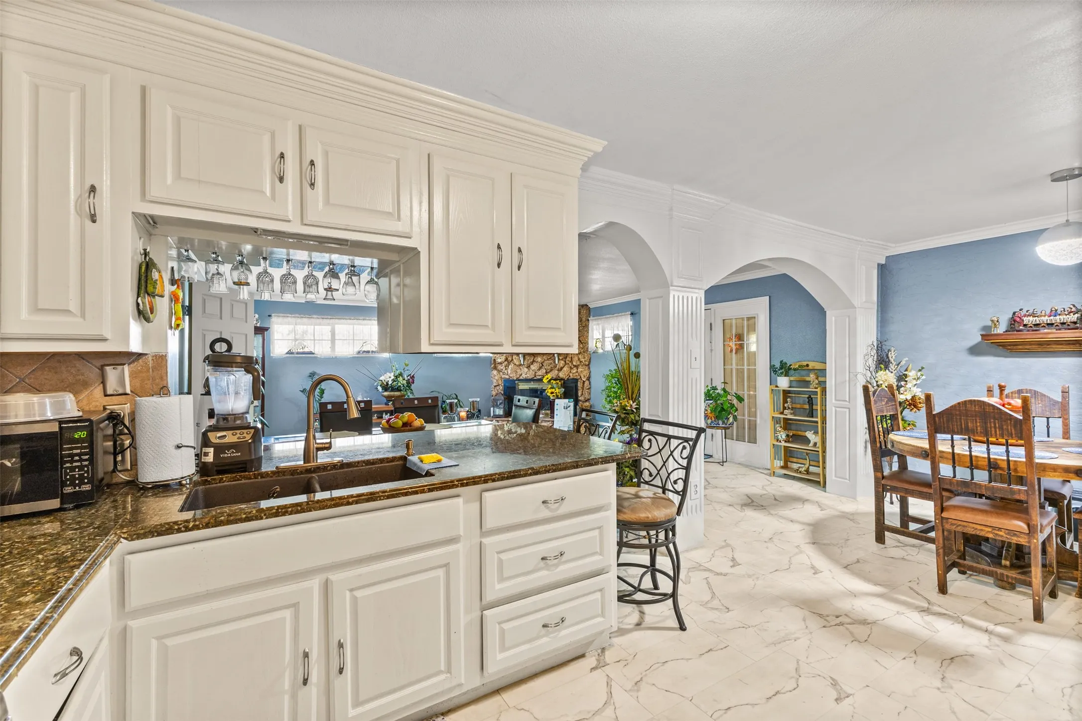 White cabinetry, stone countertops, dual-basin sink, stone tile flooring, and decorative archways