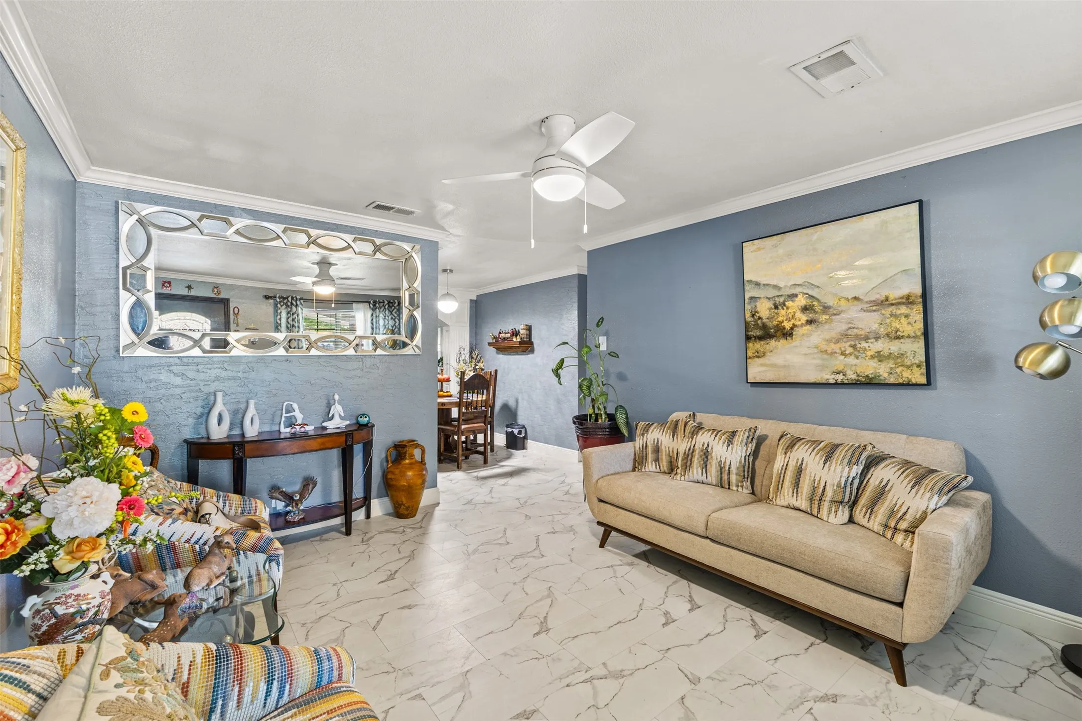 Living area featuring stone-finish tile flooring, crown molding, and a central ceiling fan with integrated lighting