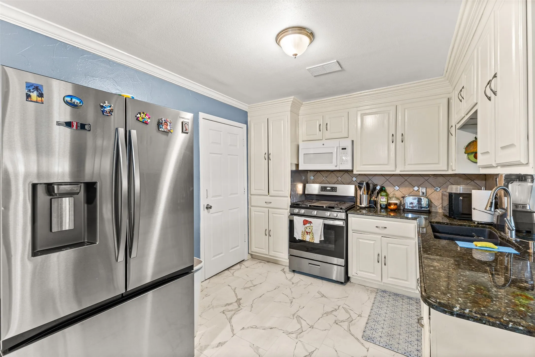 Kitchen featuring white shaker-style cabinetry, stainless steel appliances, dark stone countertops, a tiled backsplash, and stone-finish tile flooring