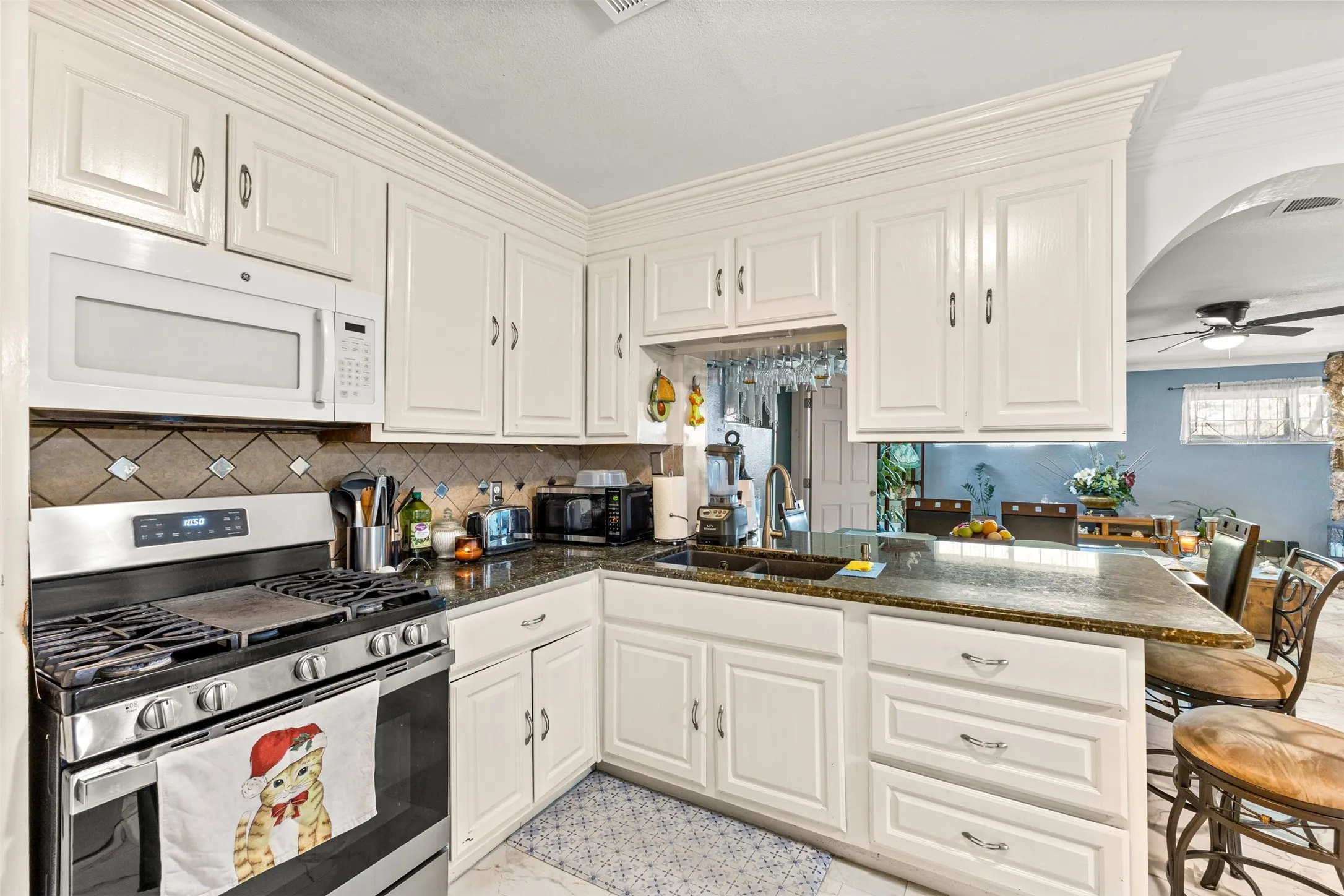 Kitchen featuring white cabinetry with crown molding, stone-finish countertops, tile backsplash, built-in microwave, and a stainless steel gas range