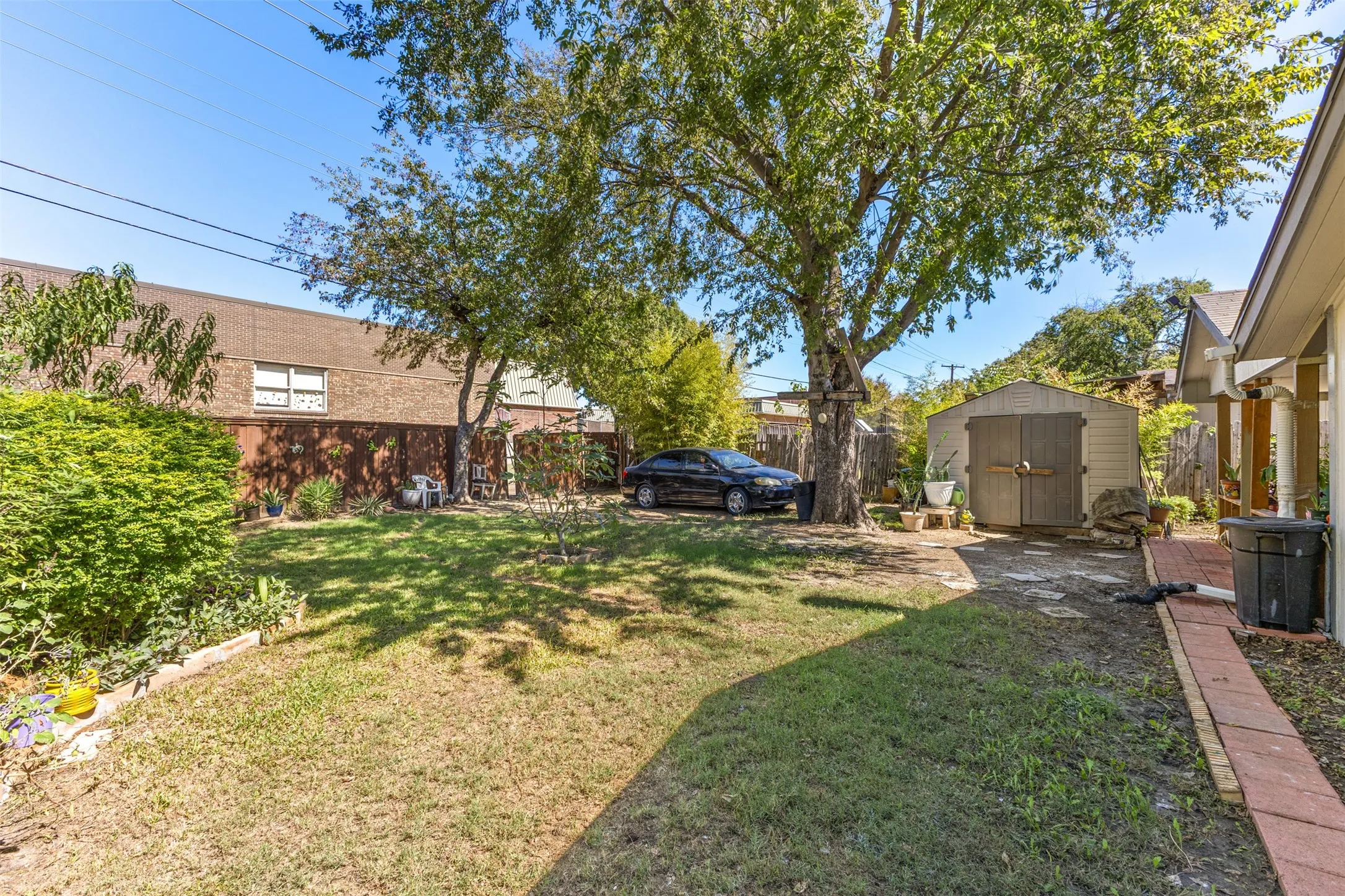 Backyard area featuring a manicured lawn, mature trees, a detached storage shed, and a brick-paver pathway