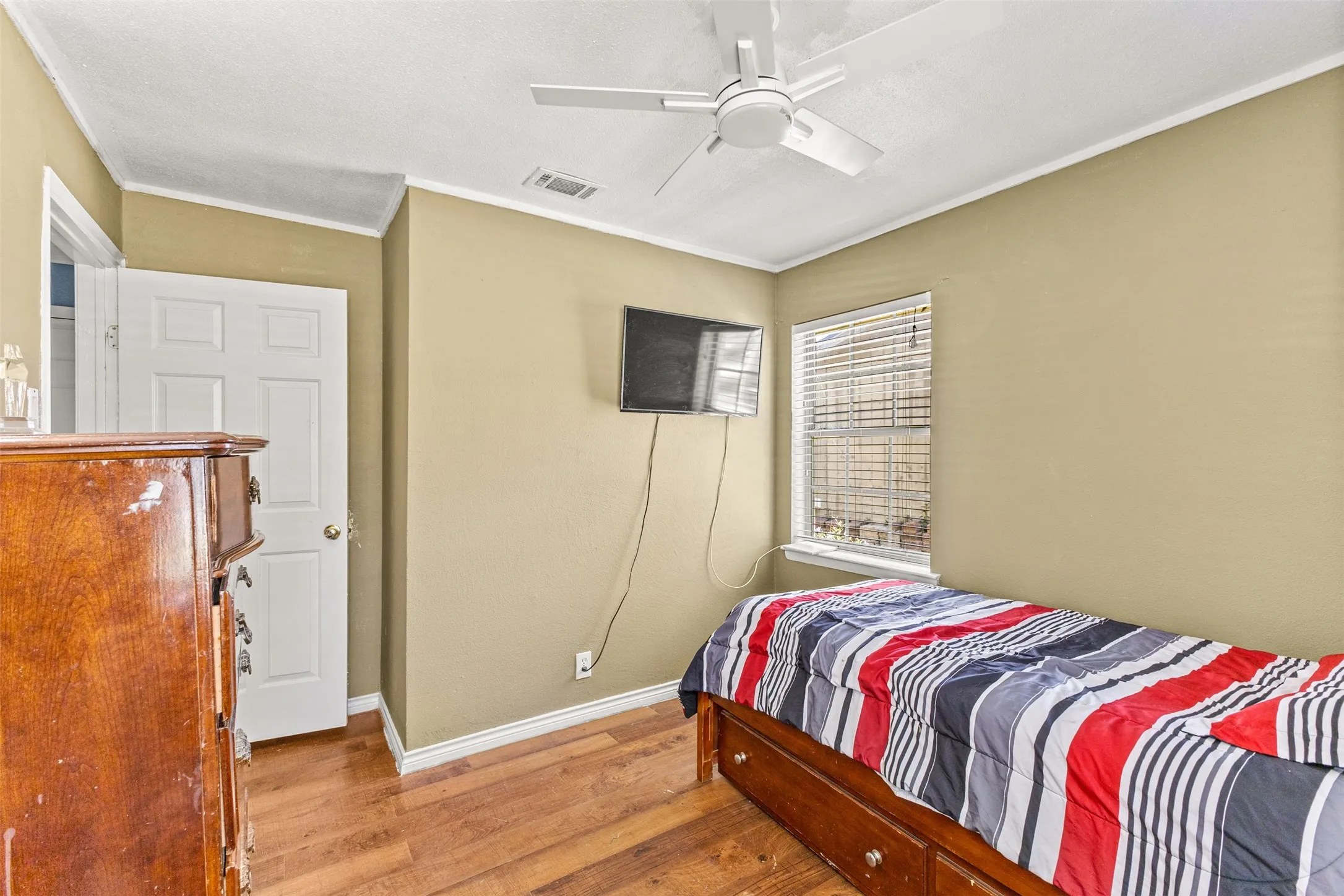 Room featuring wood-finish flooring, a ceiling fan, and a single-pane window with horizontal blinds