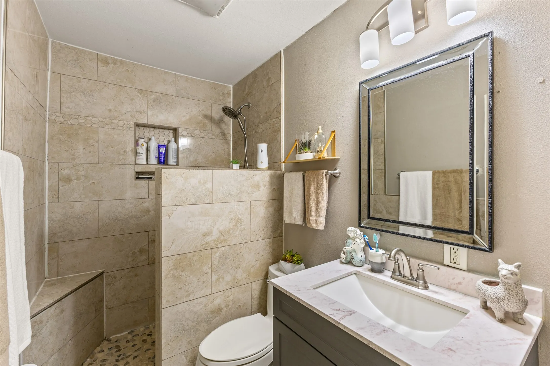 Walk-in shower with stone tile surround, built-in bench, and pebble flooring, featuring a dark-finish vanity with a white countertop and rectangular undermount sink