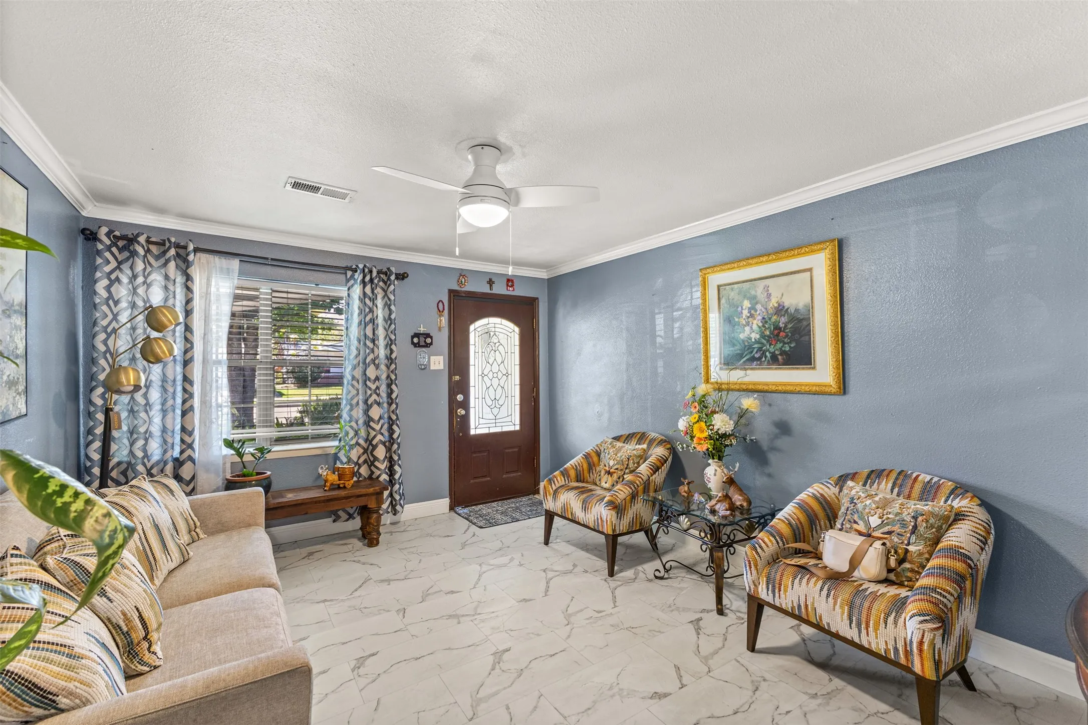 Entryway featuring stone-finish tile flooring, a solid-core front door with an ornate glass inlay, crown molding, and a central ceiling fan with integrated lighting