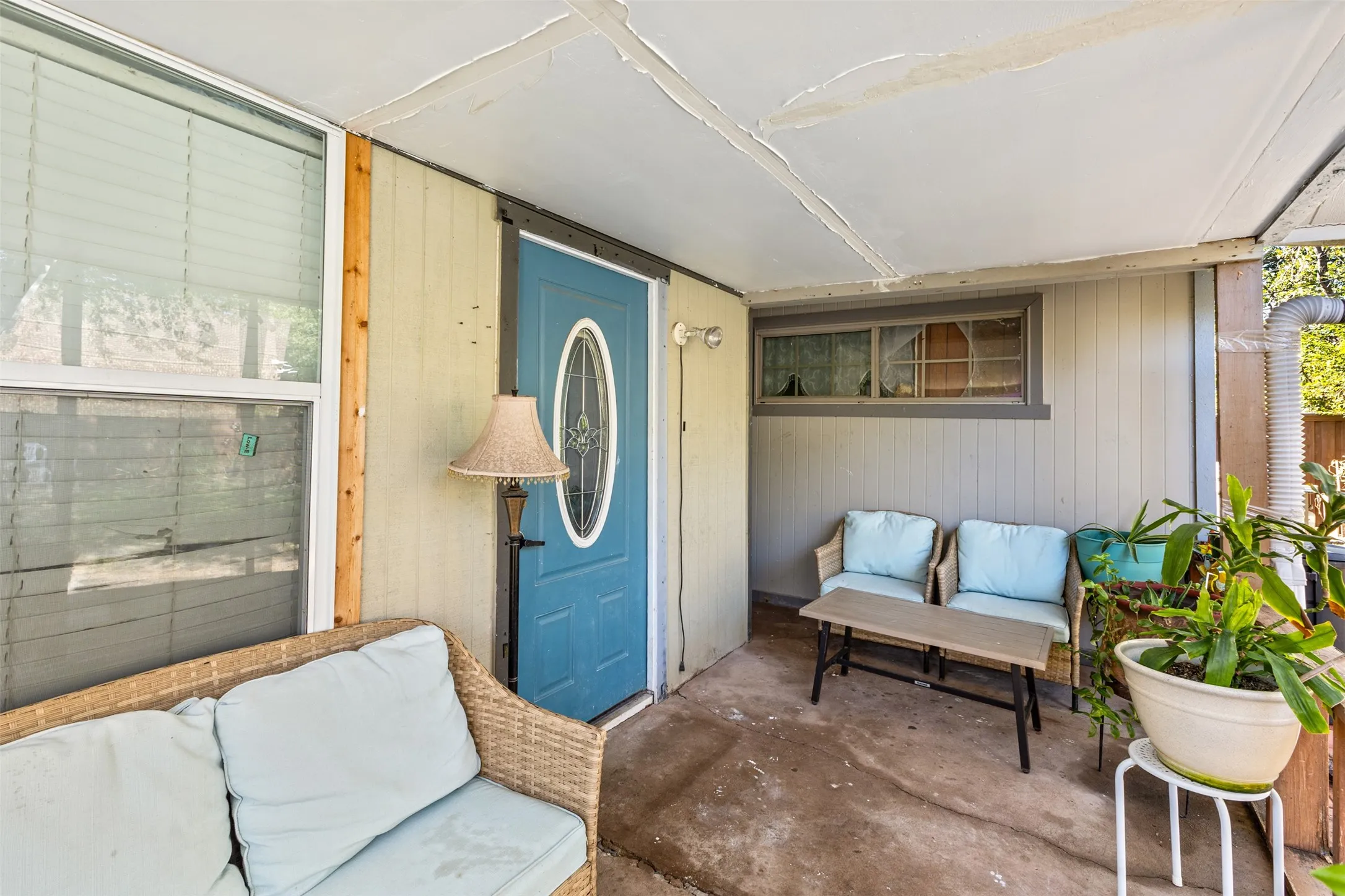 Covered front porch featuring a concrete floor, horizontal and vertical wood-style siding, and a blue exterior door with a central oval glass insert