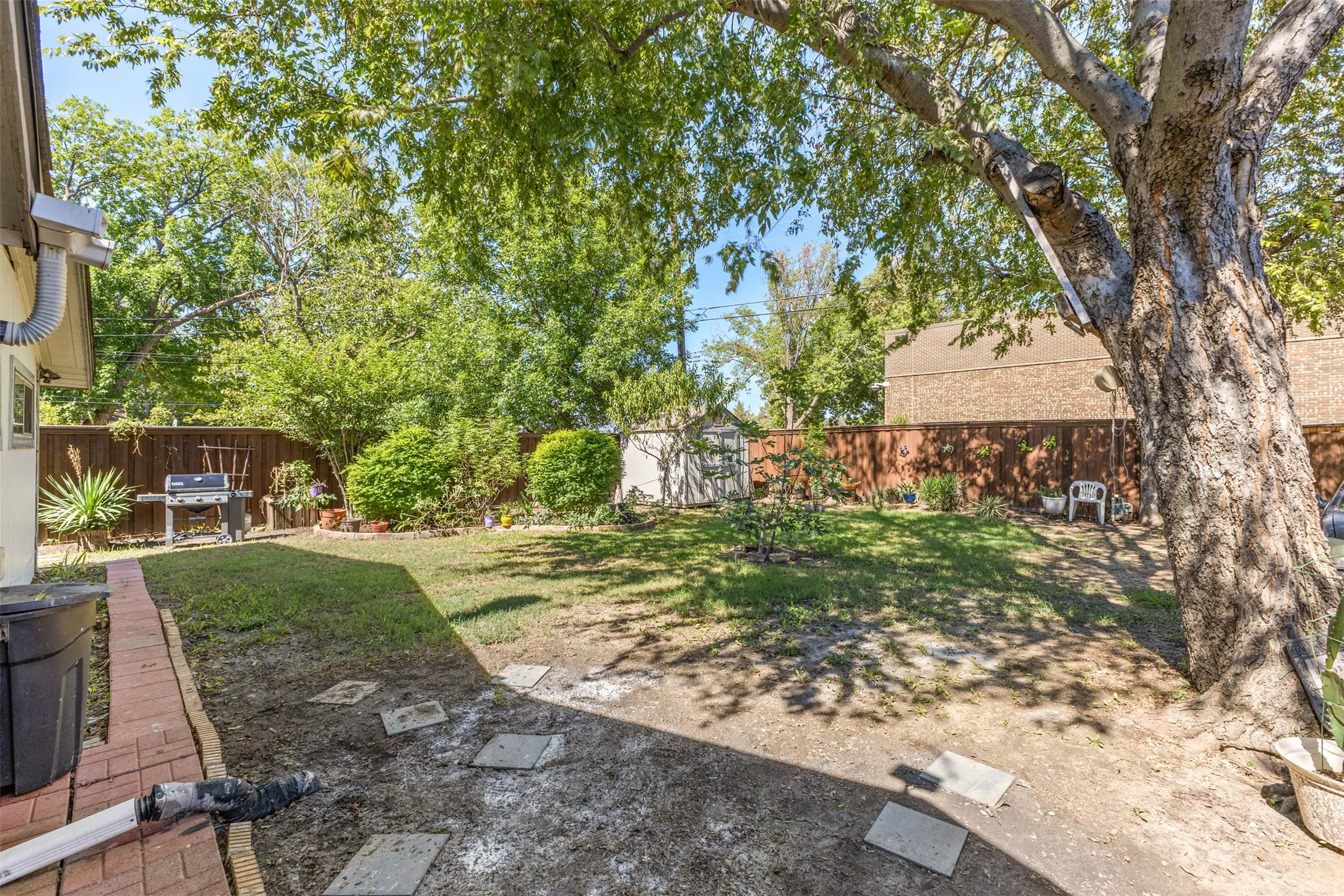 Backyard featuring a wood privacy fence, mature trees, a brick walkway, and a detached storage shed