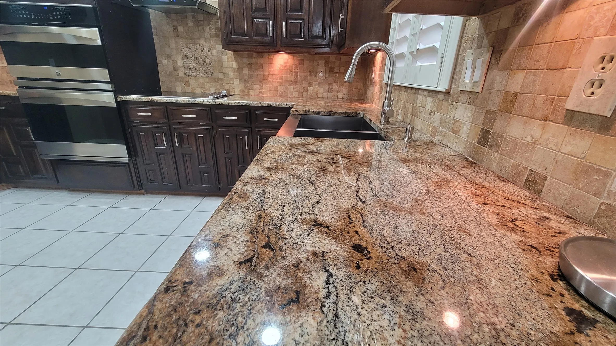 Kitchen featuring stone countertops, dark wood cabinetry, a stainless steel double wall oven, and a stone tile backsplash