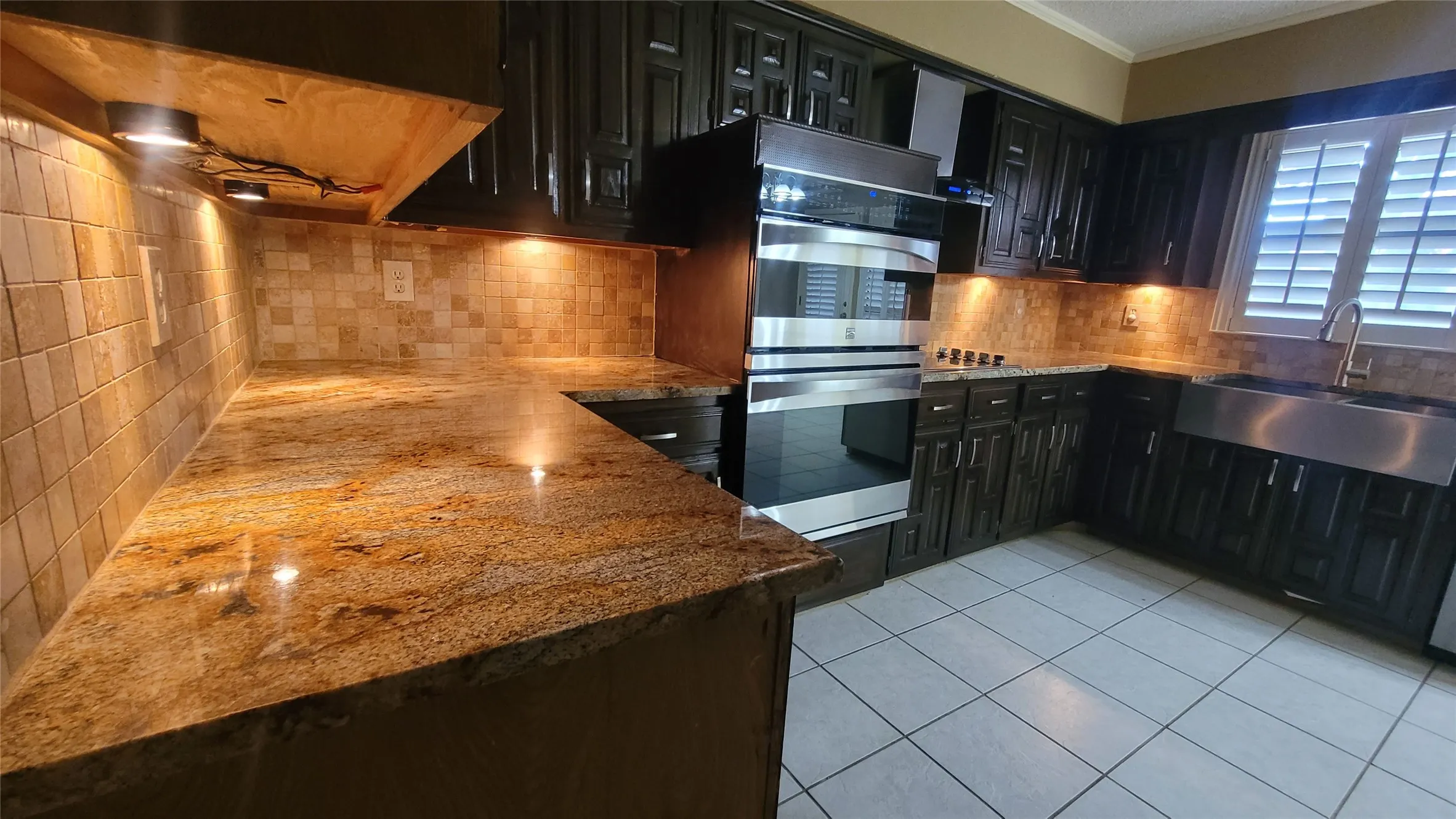 Kitchen featuring dark cabinetry, stone countertops, square-tile backsplash, built-in double wall ovens, and a stainless steel farmhouse-style sink