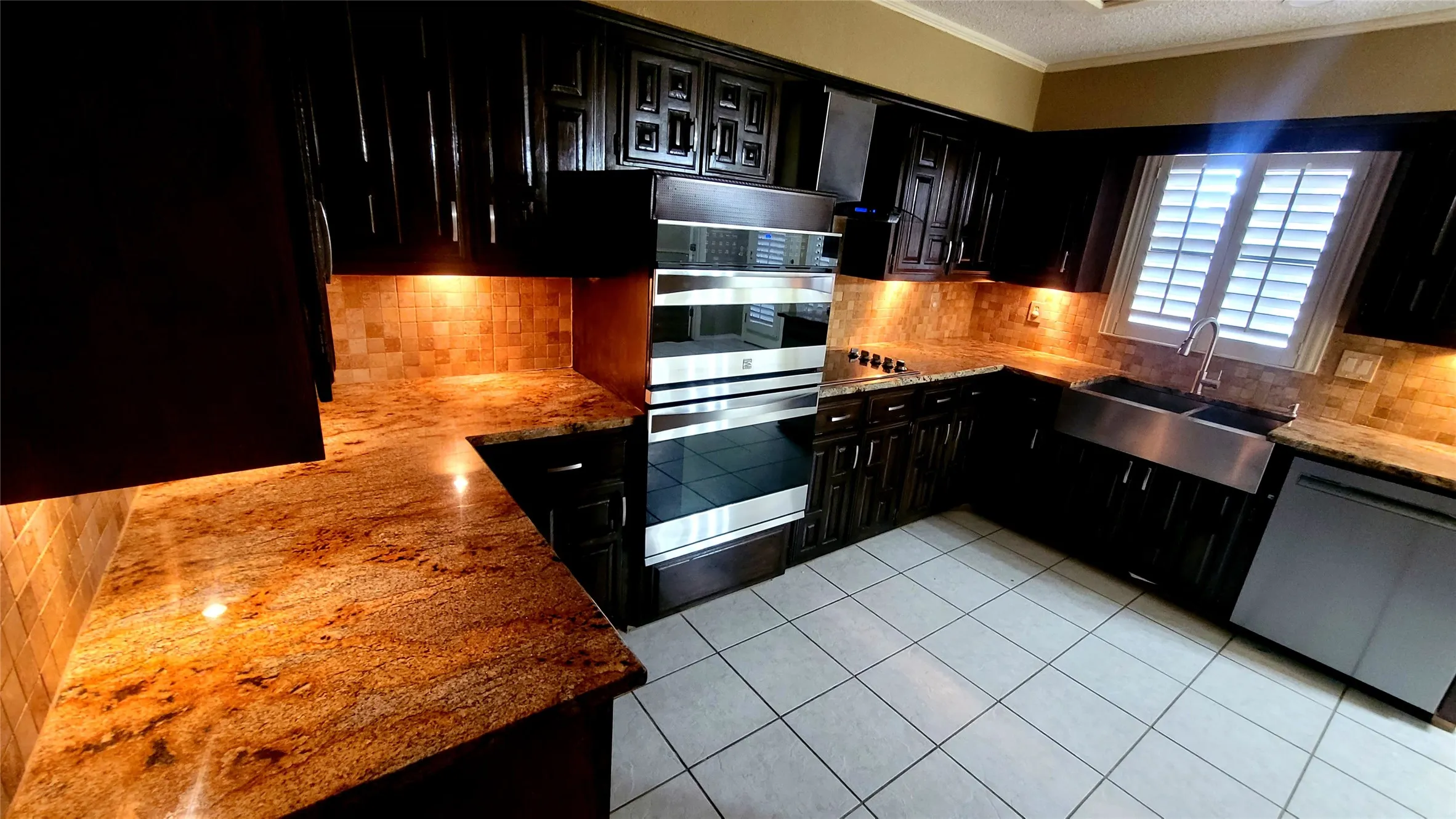 Dark wood cabinetry, stone countertops, stainless steel double wall ovens, apron-front sink, and tile flooring