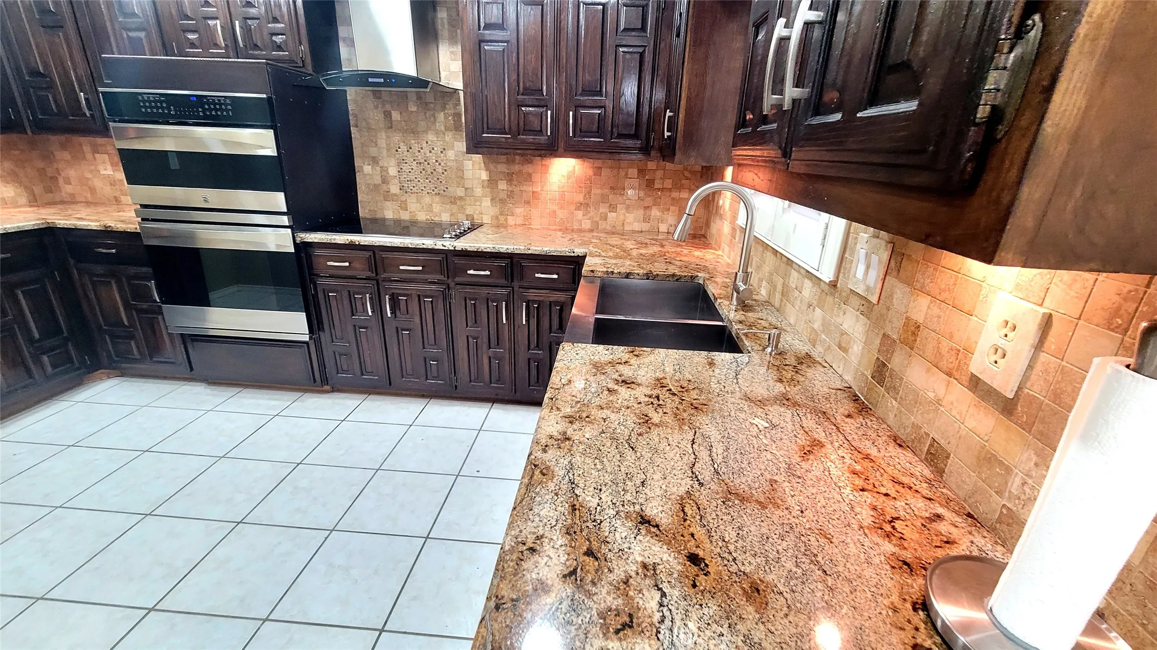 Kitchen featuring custom dark-toned wood cabinetry, stone countertops, a tiled backsplash, stainless steel double wall oven, and dual-basin undermount sink with a gooseneck faucet