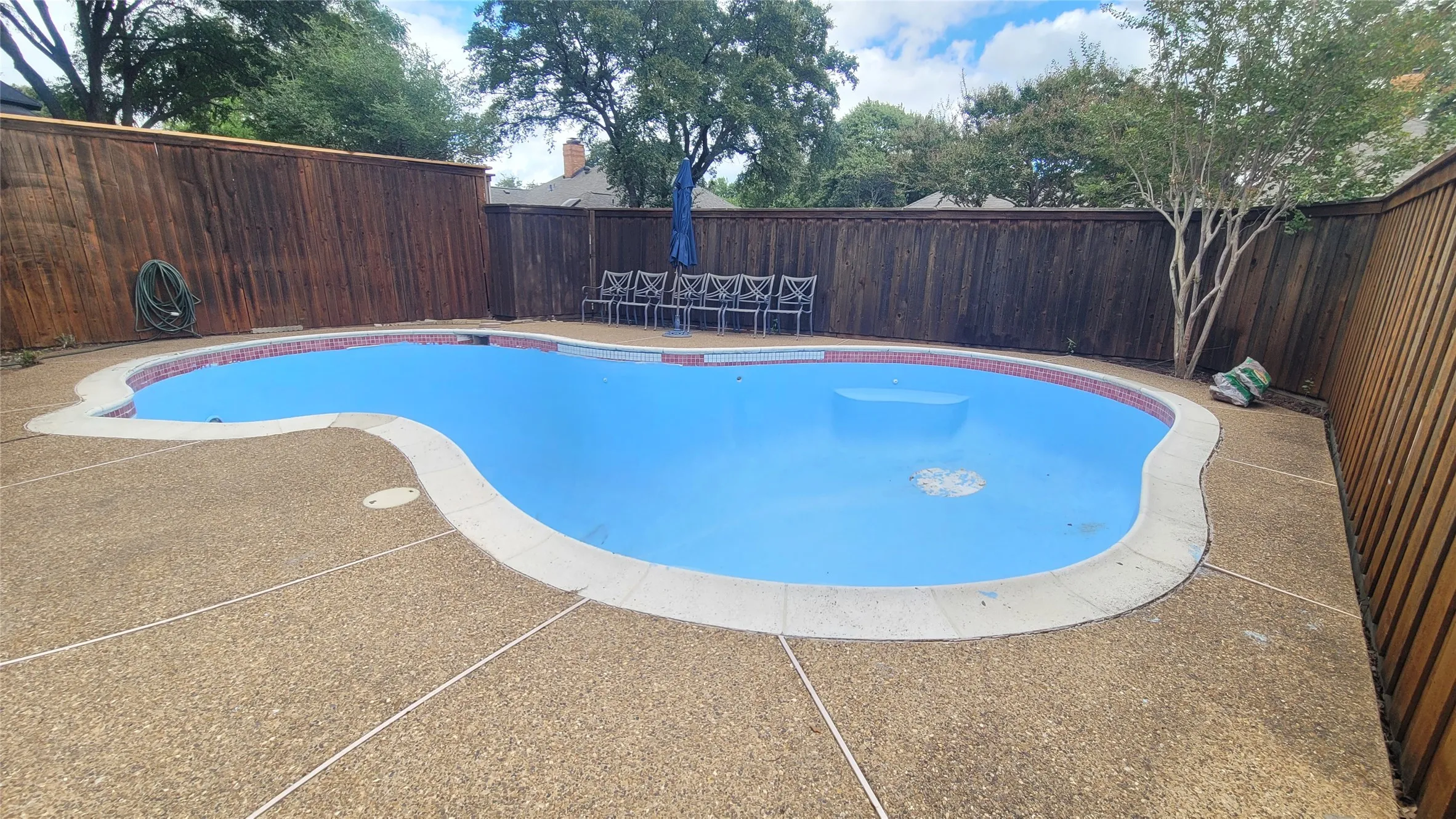 Custom-shaped in-ground pool featuring a decorative tile border, aggregate decking, and perimeter wood privacy fencing