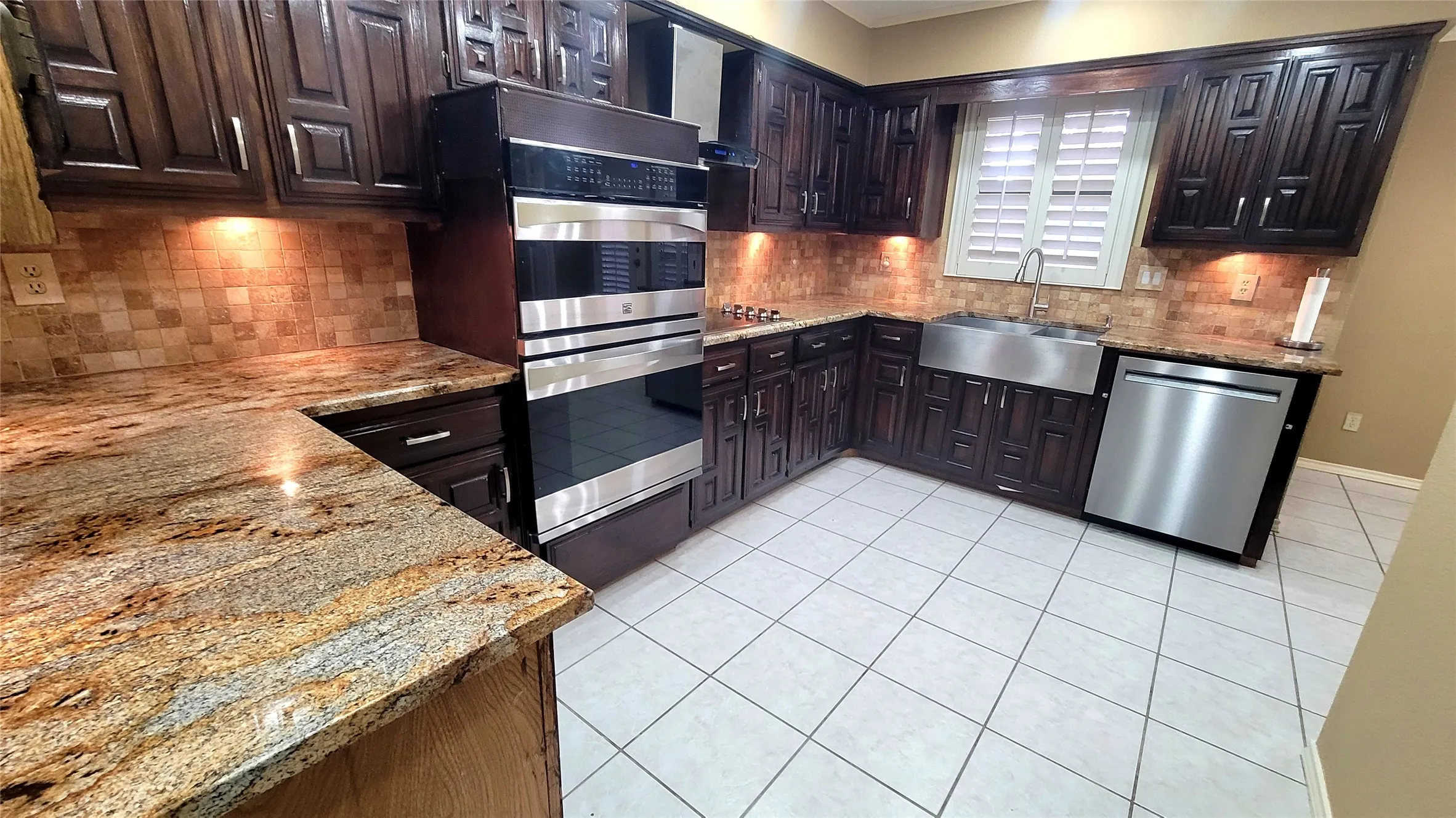 Kitchen featuring dark wood cabinetry, natural stone countertops, stainless steel farmhouse sink, built-in double wall oven, and ceramic tile flooring