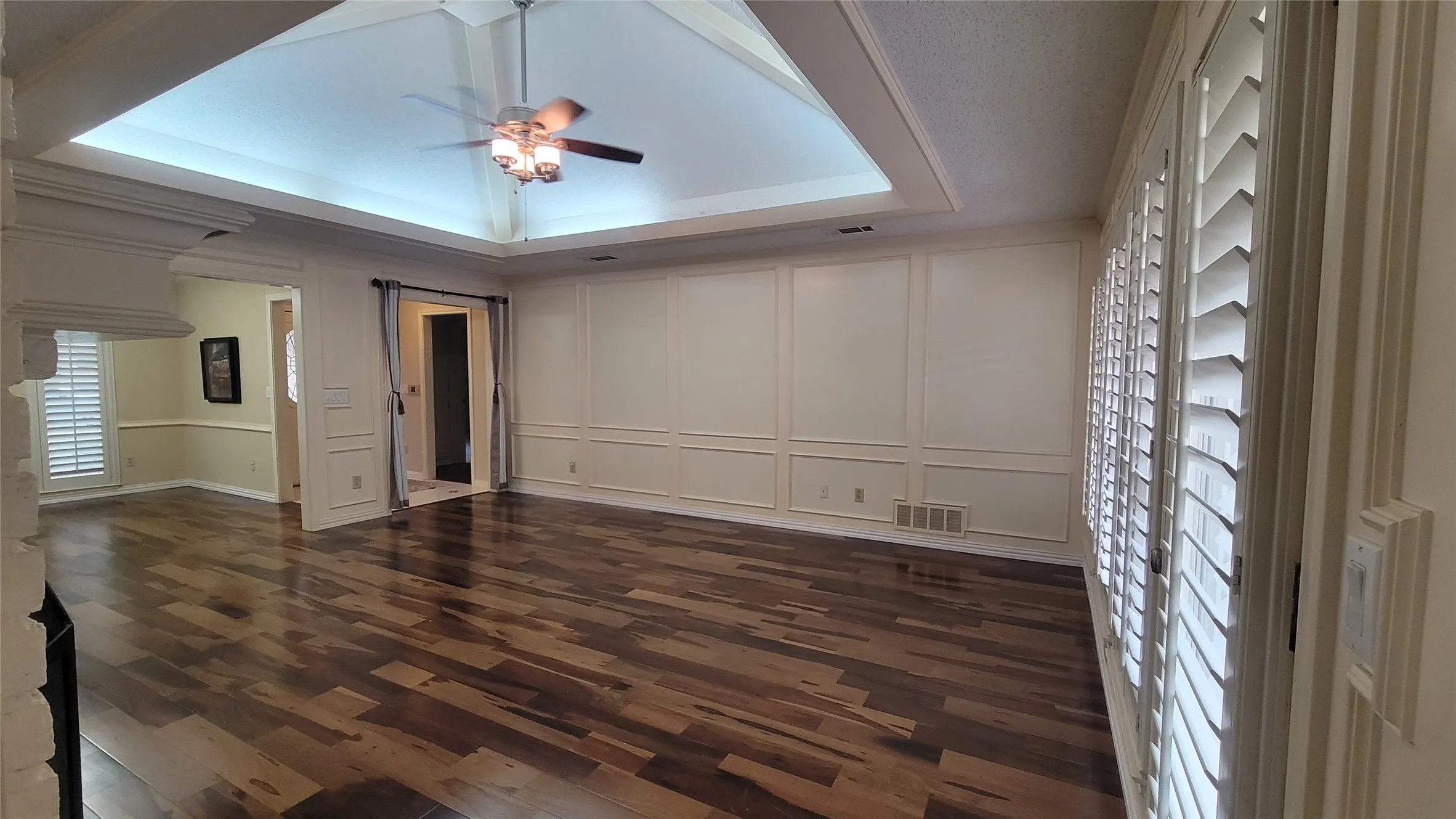 Vaulted tray ceiling with recessed lighting, wood-finish flooring, wainscot wall paneling, and interior plantation shutters