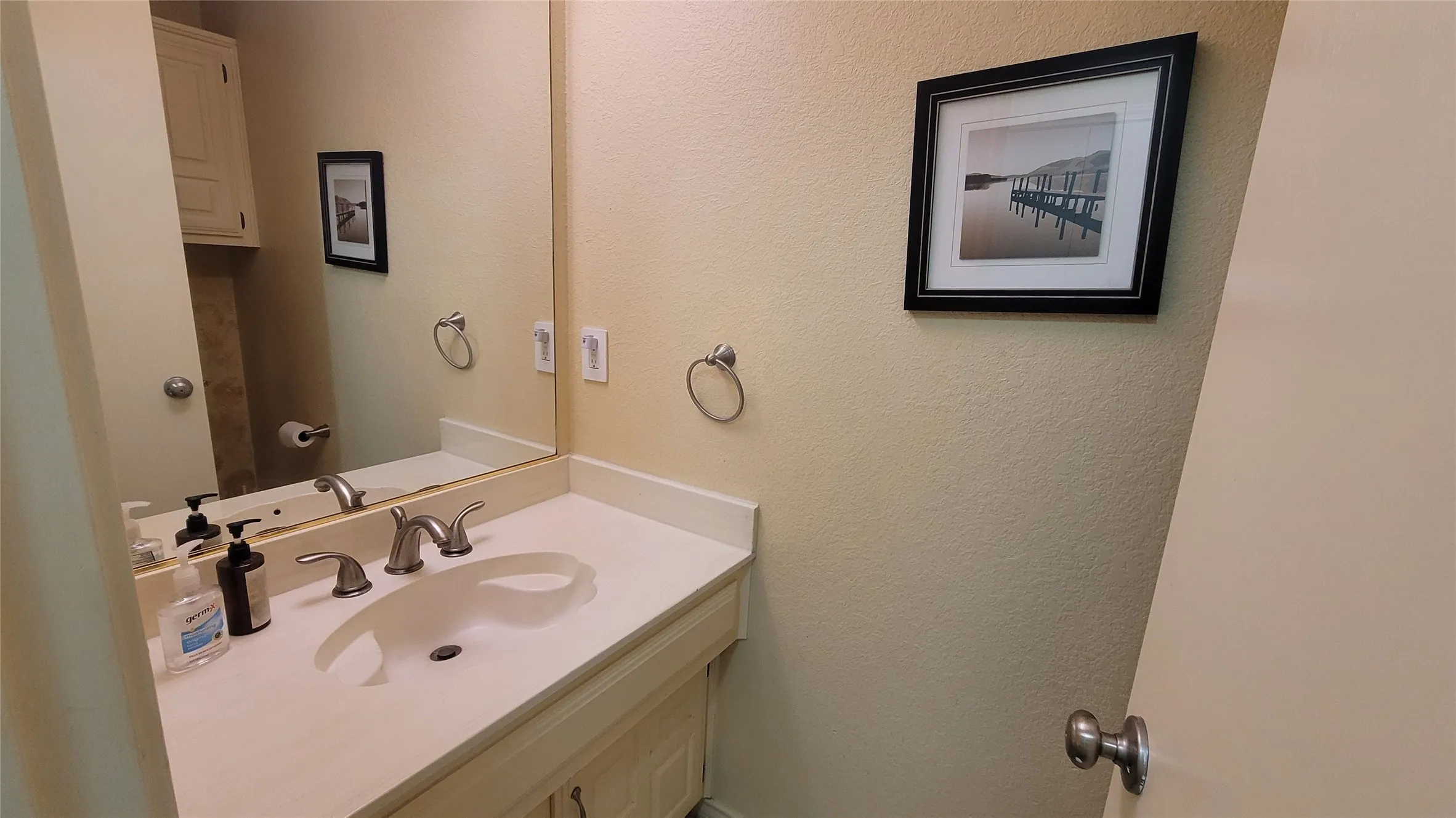 Vanity featuring a neutral countertop with an integrated basin, dual-handle metal faucet, wall-mounted mirror, and cabinet storage