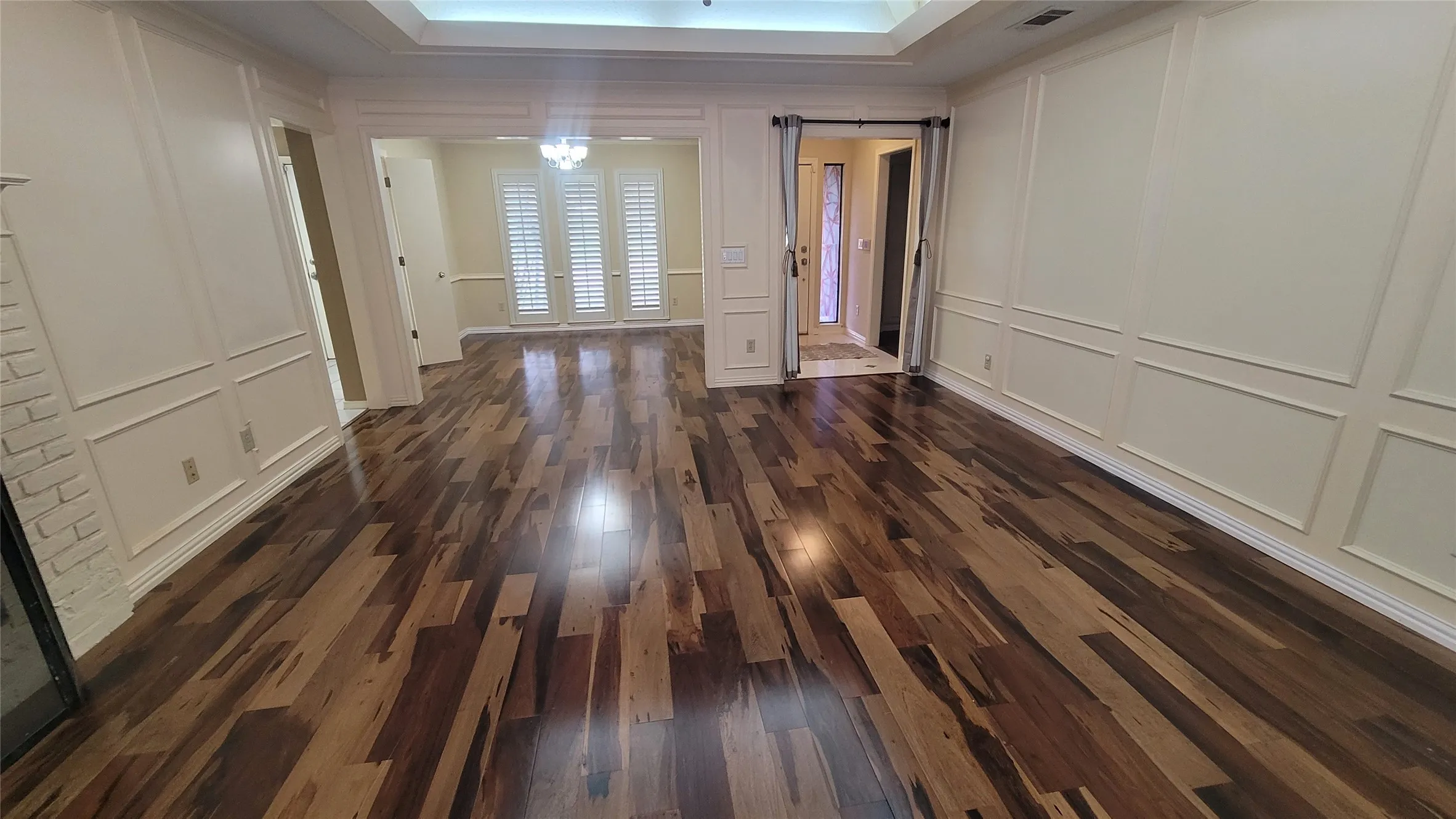 Interior featuring multi-tonal wood-finish flooring, wainscoting wall paneling, a tray ceiling, and shutter-style window coverings